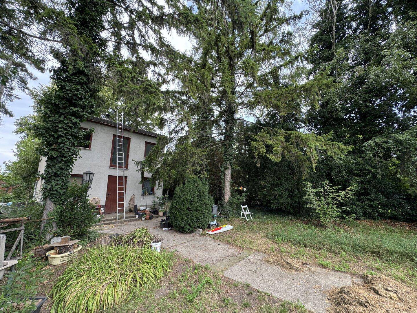 Einfaches zweistöckiges Haus, umgeben von Bäumen und Vegetation, mit einer Leiter an der Fassade.