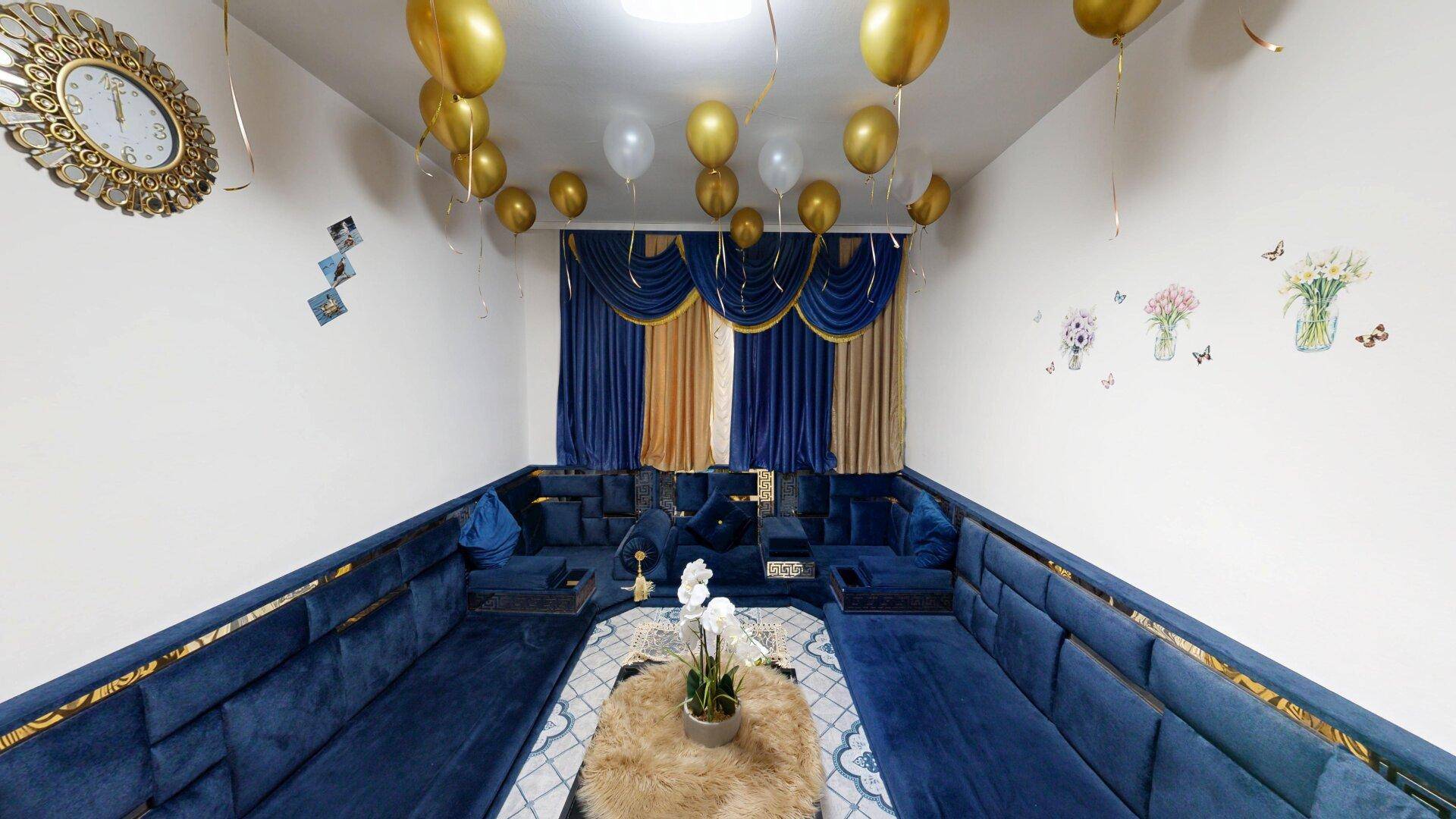 Wohnzimmer mit traditionellen blauen Sitzgelegenheiten, einem Couchtisch und festlicher Ballondekoration.