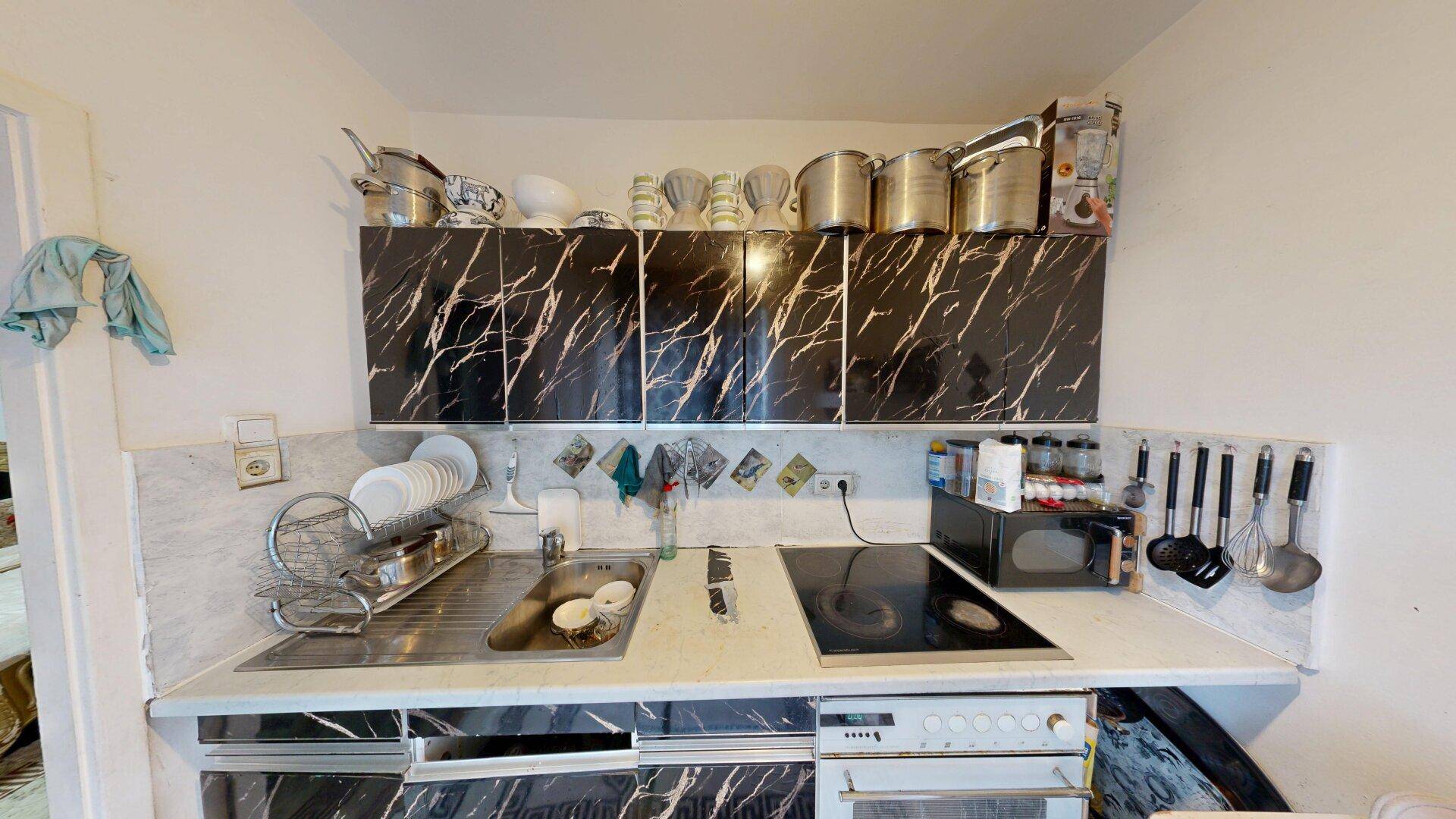 Funktionale Küche mit Spülbecken, Kochfeld und Backofen unter den Marmor-Effekt-Arbeitsplatten.