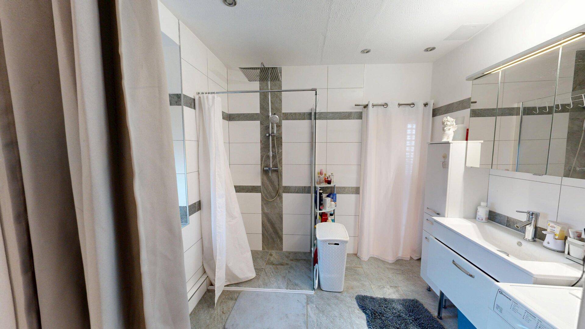 Modernes Badezimmer mit großen Fliesen, ebenerdiger Dusche und Doppelwaschbecken.