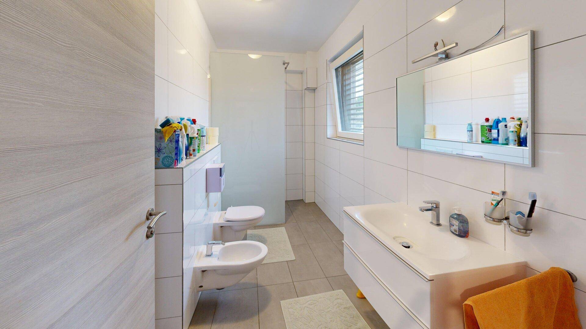 Modernes Badezimmer mit Dusche, Bidet, Einzelwaschbecken und hellen Fliesen.