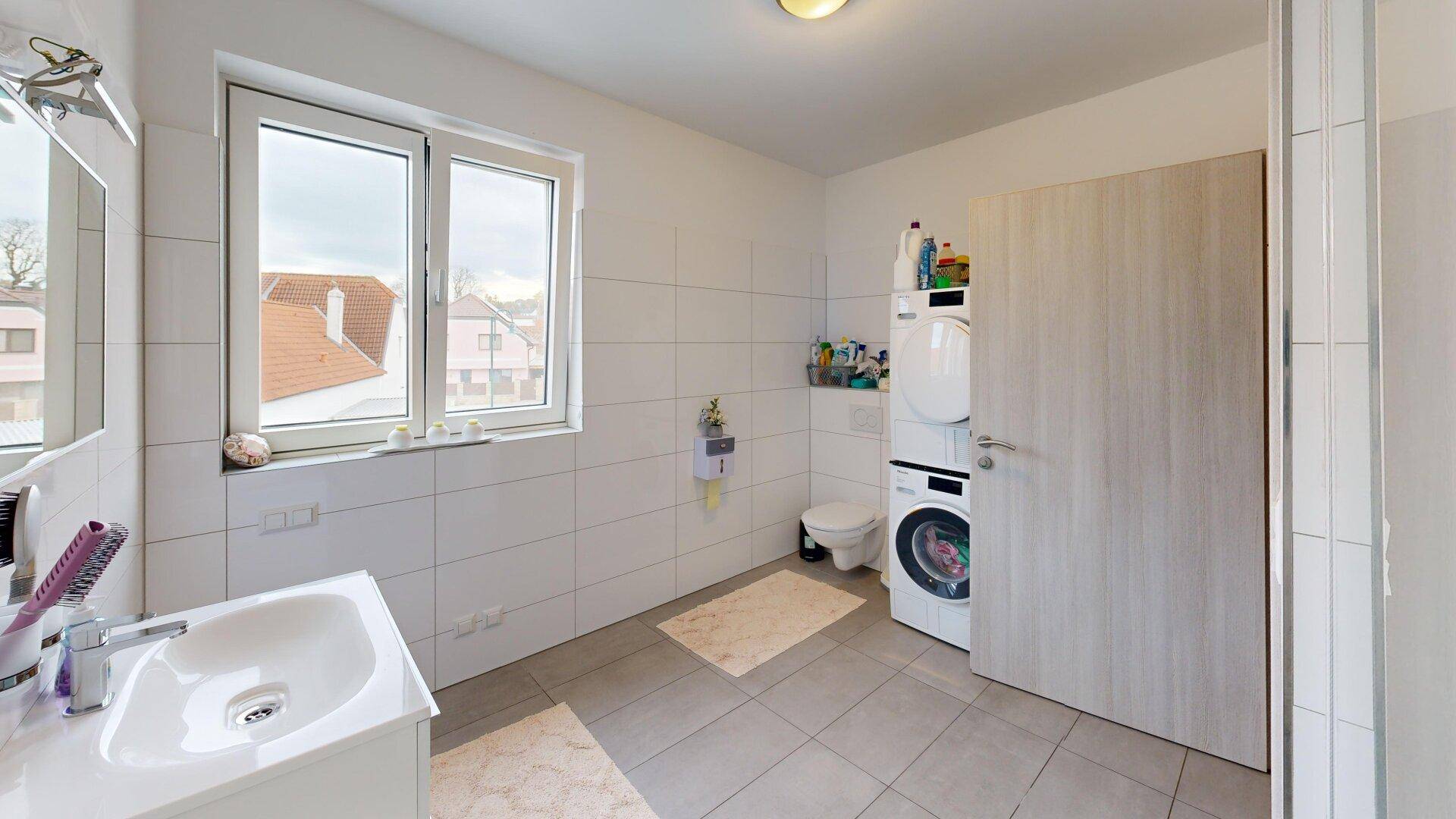 Helles Badezimmer mit Fenster, Waschmaschine und Trockner, sowie modernem Waschbecken.