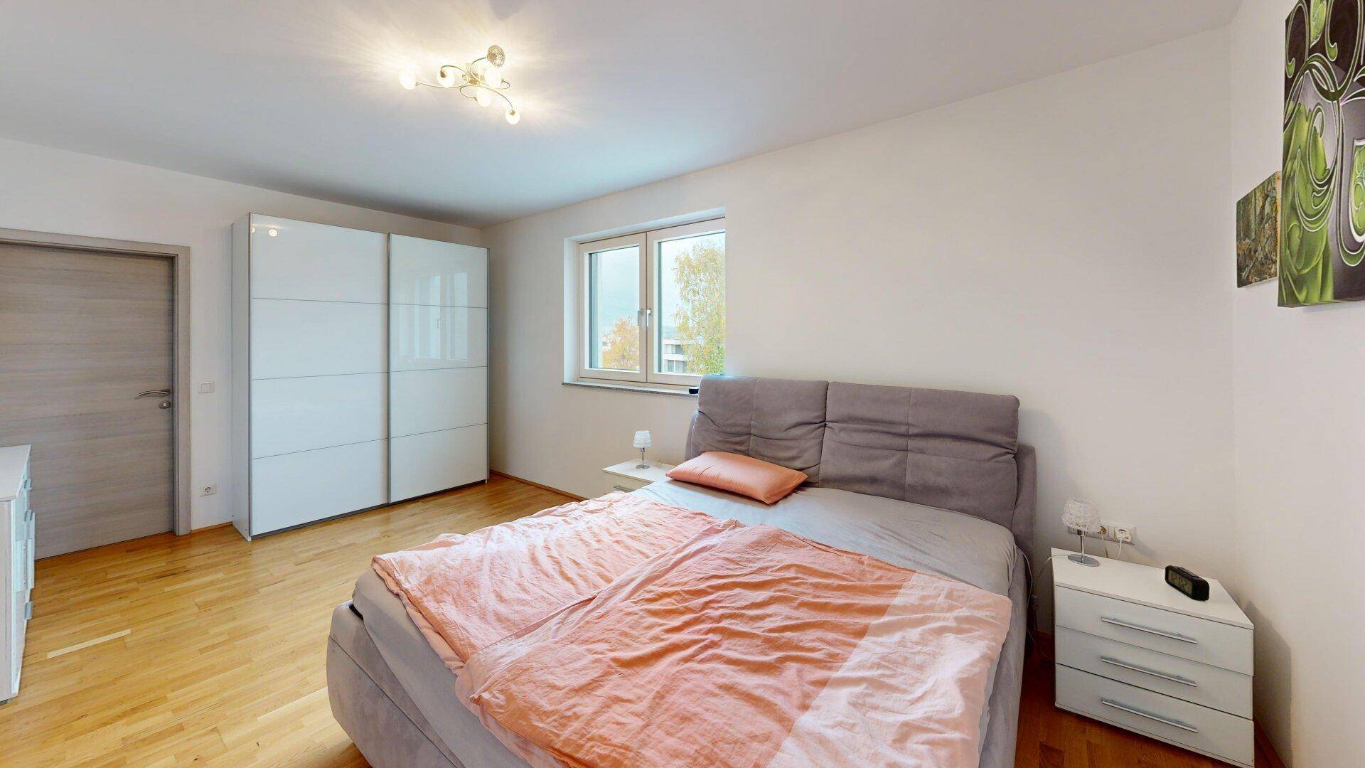 Helles Schlafzimmer mit Doppelbett, großem Kleiderschrank und Parkettboden.