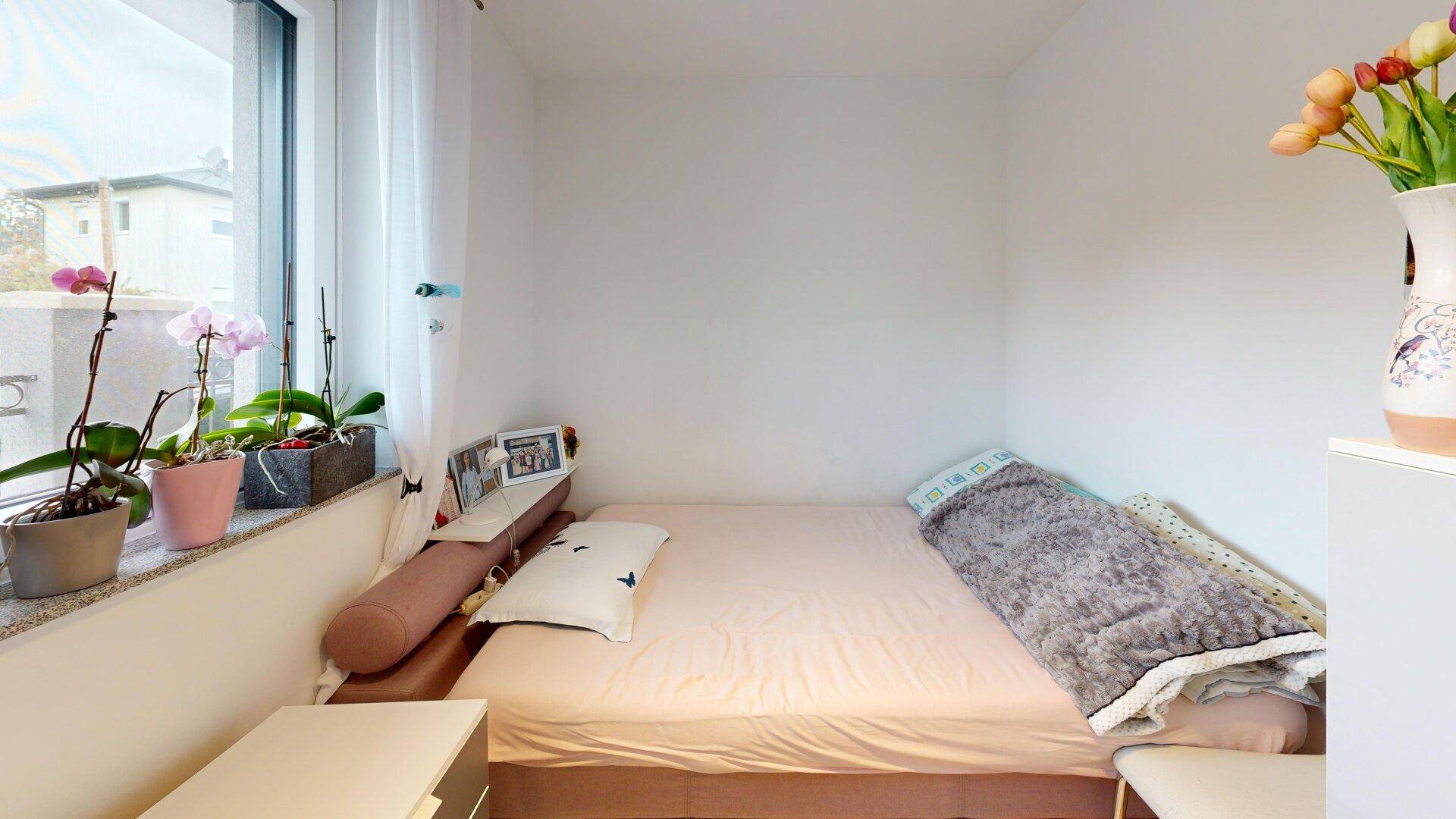 Kleines Schlafzimmer mit Einzelbett und Fensterbank, dekoriert mit Pflanzen.
