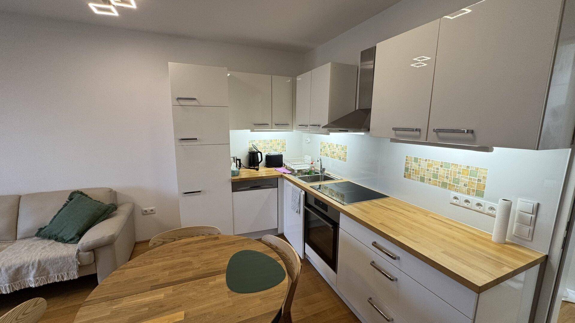 Moderne Einbauküche mit weißen Hochglanzfronten, Holzarbeitsplatte und Fliesenrückwand.