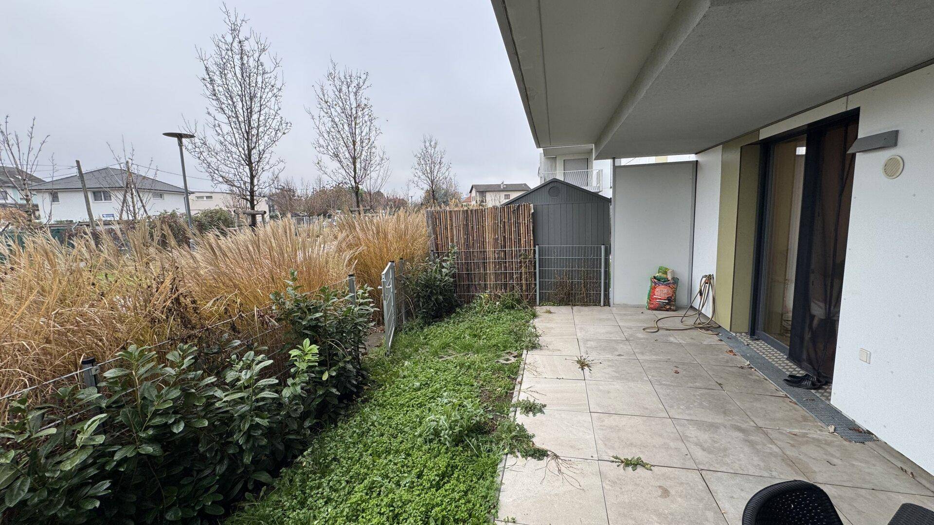 Geräumige Terrasse mit angrenzendem Gartenbereich und einem kleinen Geräteschuppen.