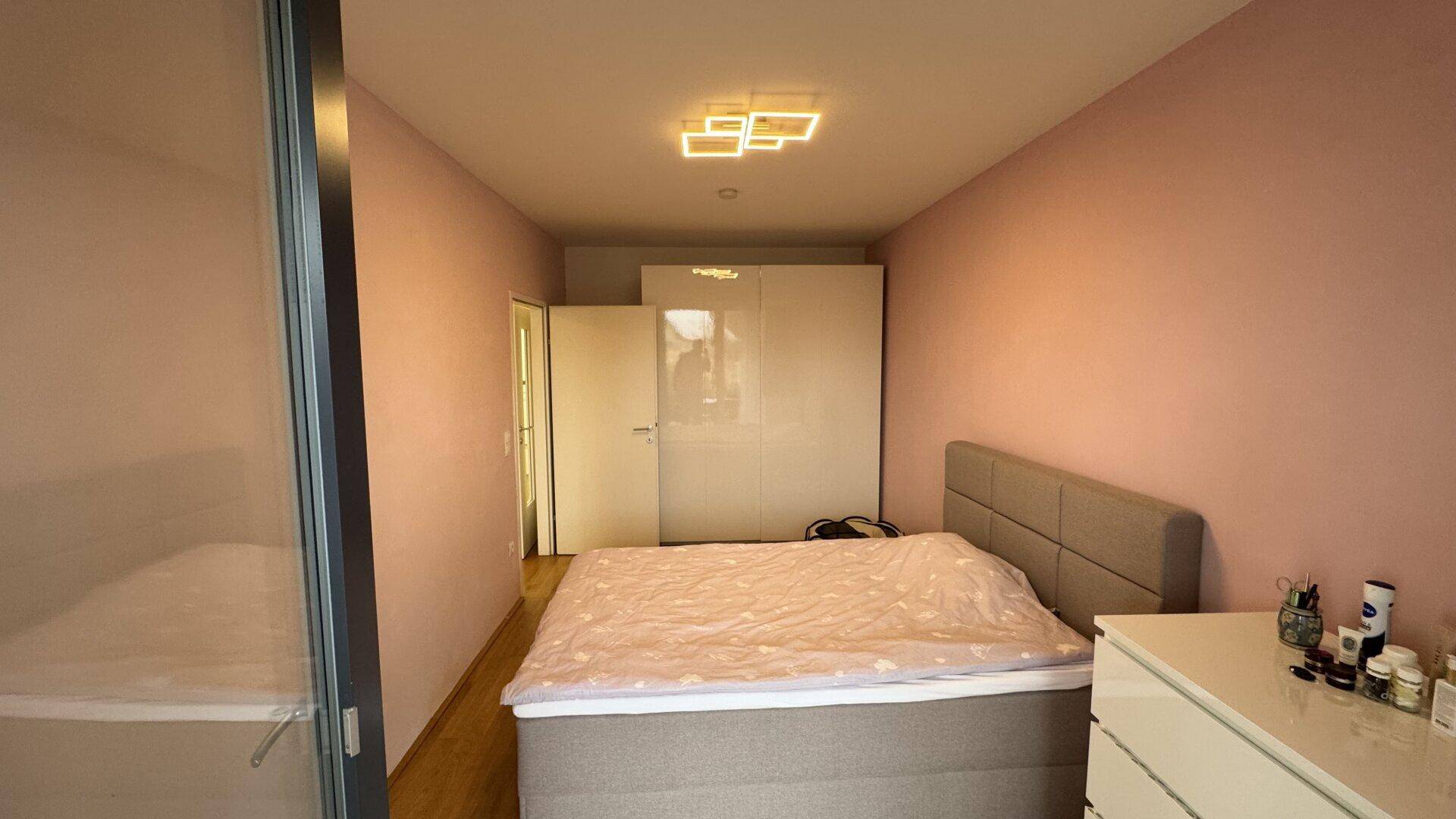 Schlafzimmer mit rosafarbenen Wänden, Doppelbett und weißem Kleiderschrank.