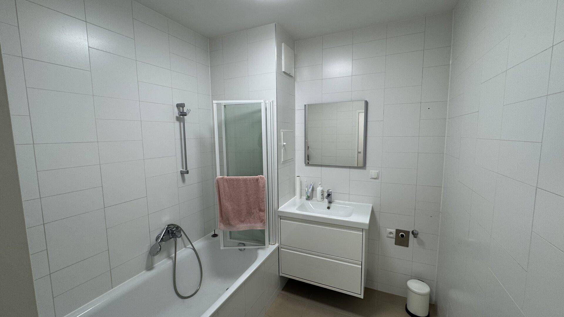 Modernes Badezimmer mit weißen Fliesen, Badewanne mit Duschfunktion und Waschbecken.
