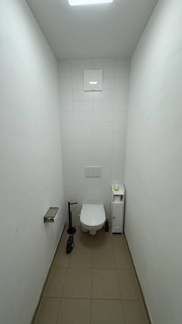 Separates WC mit weißen Wandfliesen und Bodenfliesen in neutralem Farbton.