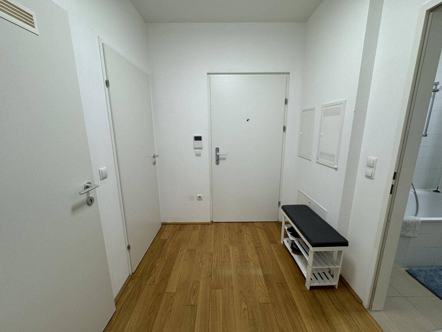 Heller Eingangsbereich mit Holzboden, weißer Tür und einer Sitzbank mit Schuhregal.