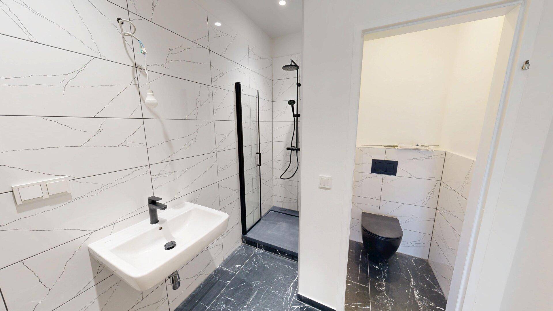 Modernes Badezimmer mit weiß-marmorierten Fliesen, schwarzer Dusche und separatem WC-Bereich.