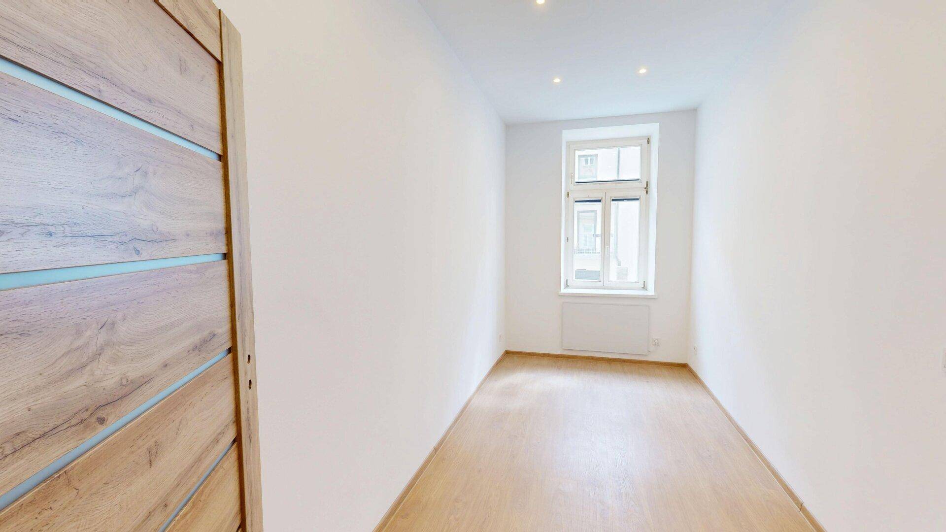 Kleineres, helles Zimmer mit einem Fenster und Holzfußboden, geeignet als Schlaf- oder Arbeitszimmer.