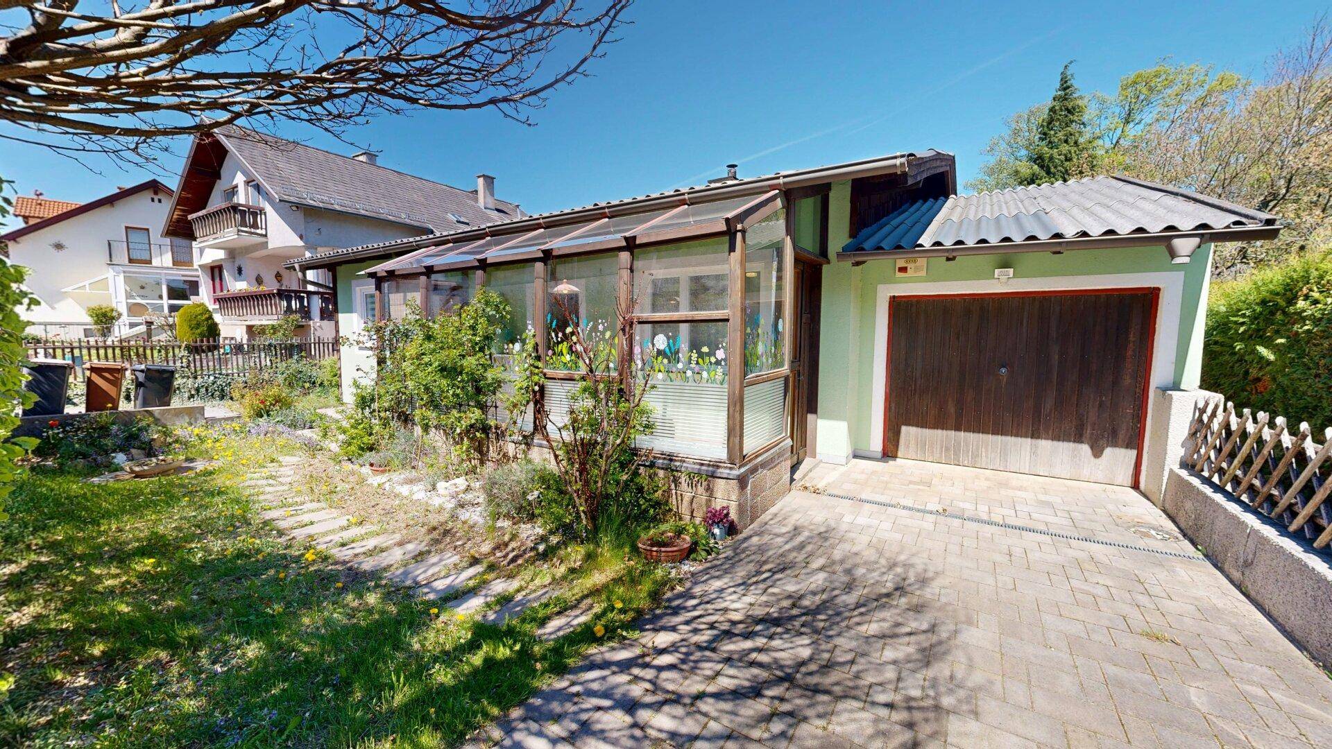 Hausfassade mit Wintergarten, Garage und gepflasterter Einfahrt.
