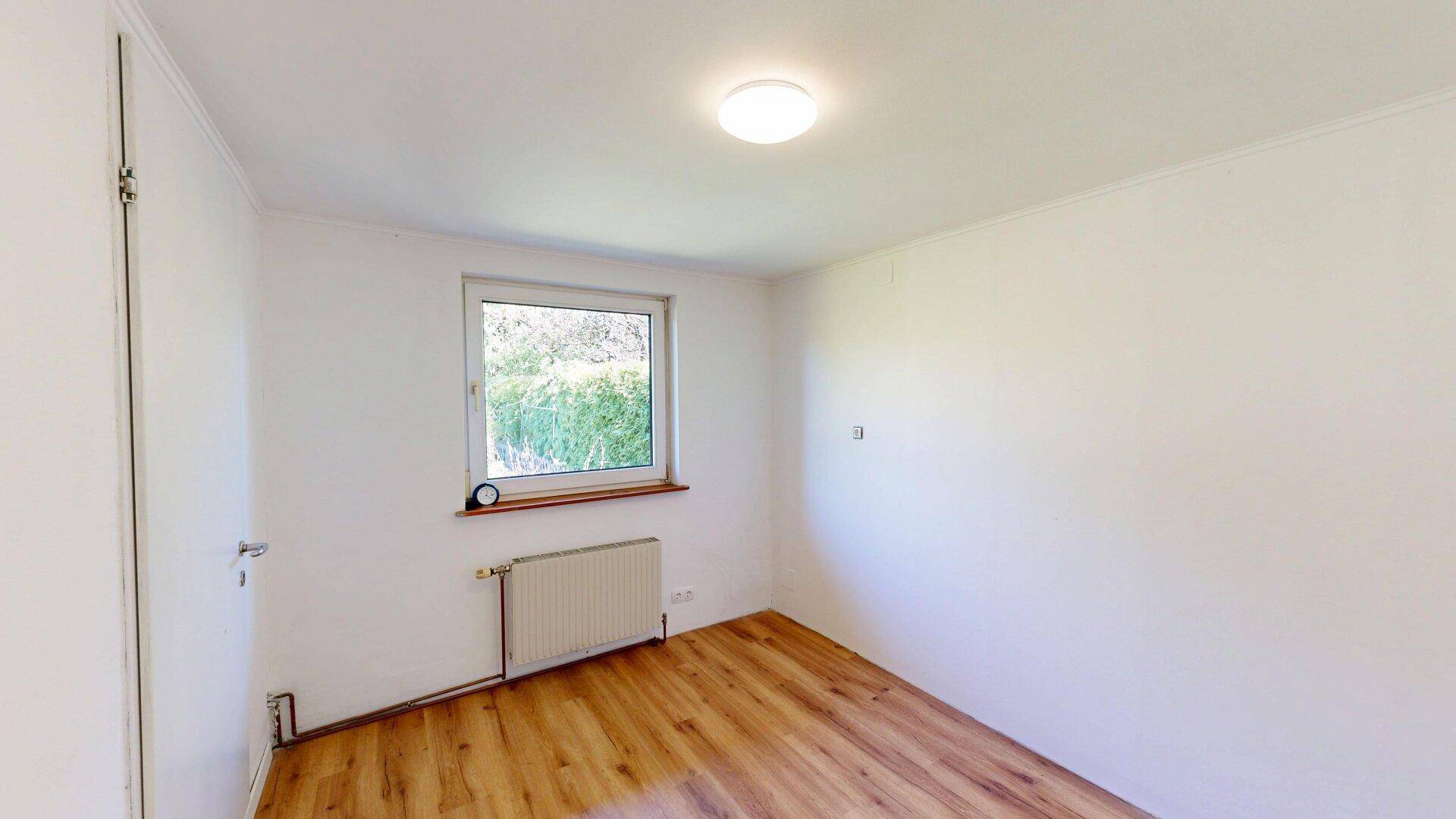 Helles Schlafzimmer mit Laminatboden, Fenster und Heizkörper für gemütliche Atmosphäre.