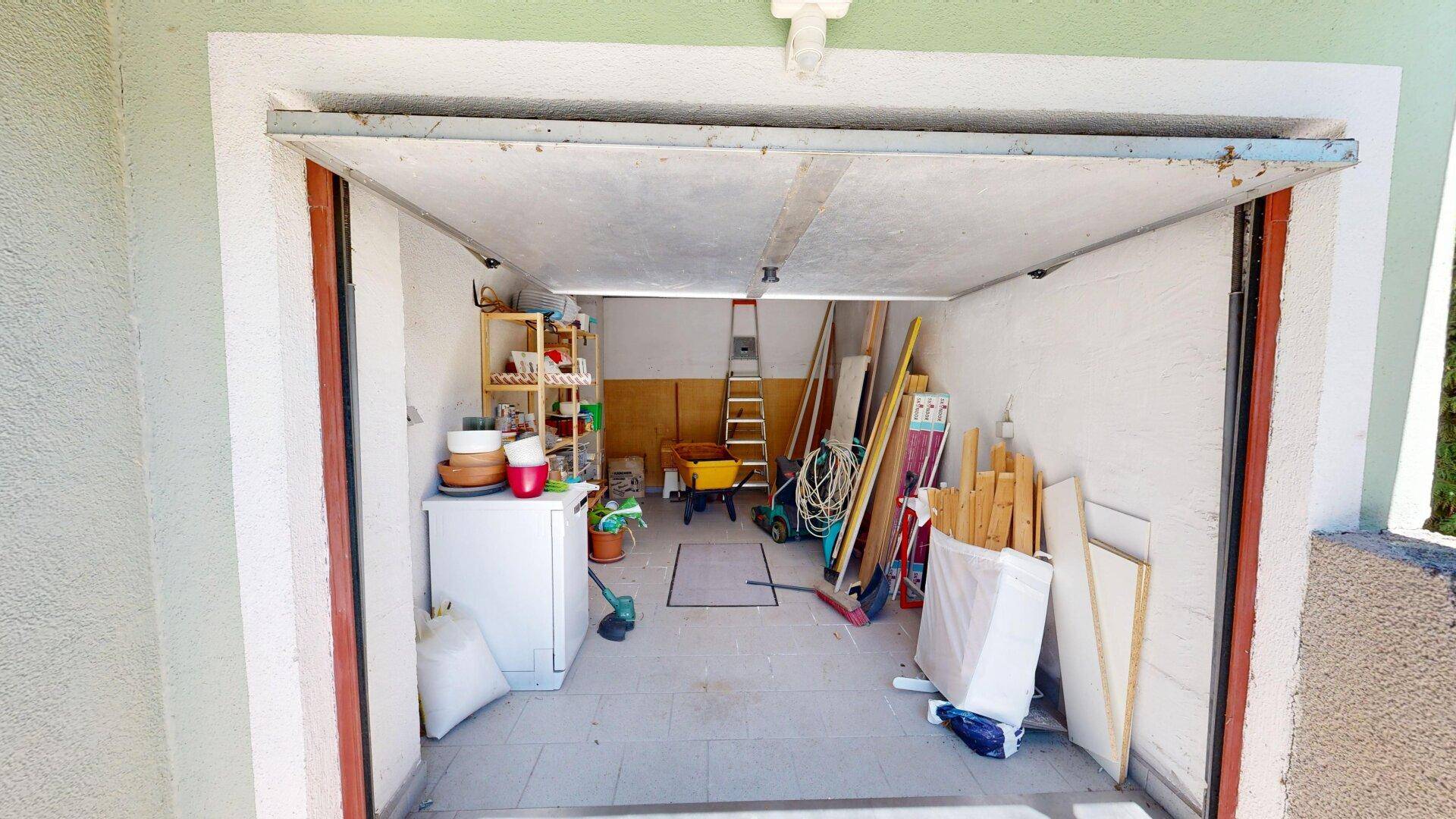 Garage mit geöffnetem Tor, Stauraum und verschiedenen Werkzeugen.
