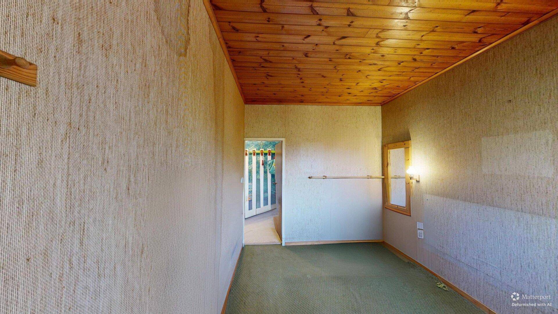 Schlafzimmer mit Teppichboden, Holzdecke und einfacher Einrichtung.
