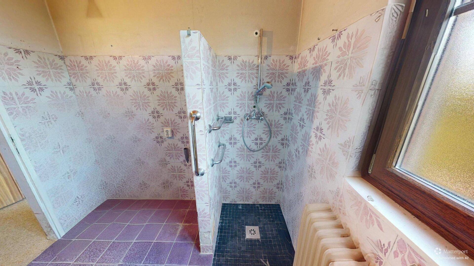 Duschbereich im Badezimmer mit farbigen Fliesen und Haltegriffen.