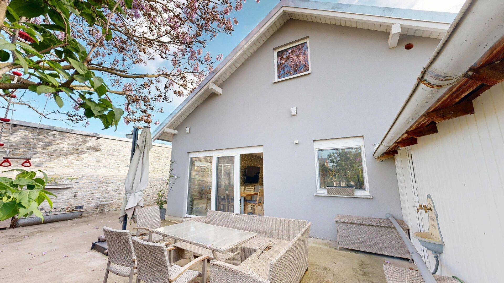 Gemütliche Terrasse mit Gartenmöbeln und Blick auf die graue Hausfassade und den Garten.