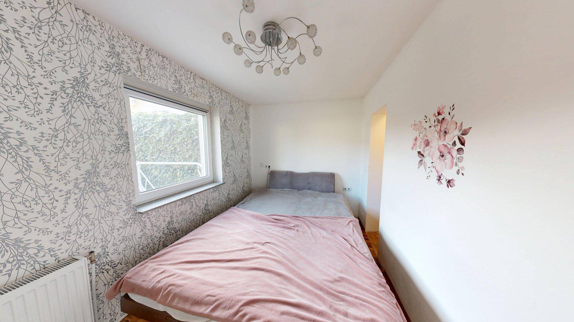 Schlafzimmer mit gemütlichem Bett, gemusterter Tapete und einem Fenster für natürliches Licht.