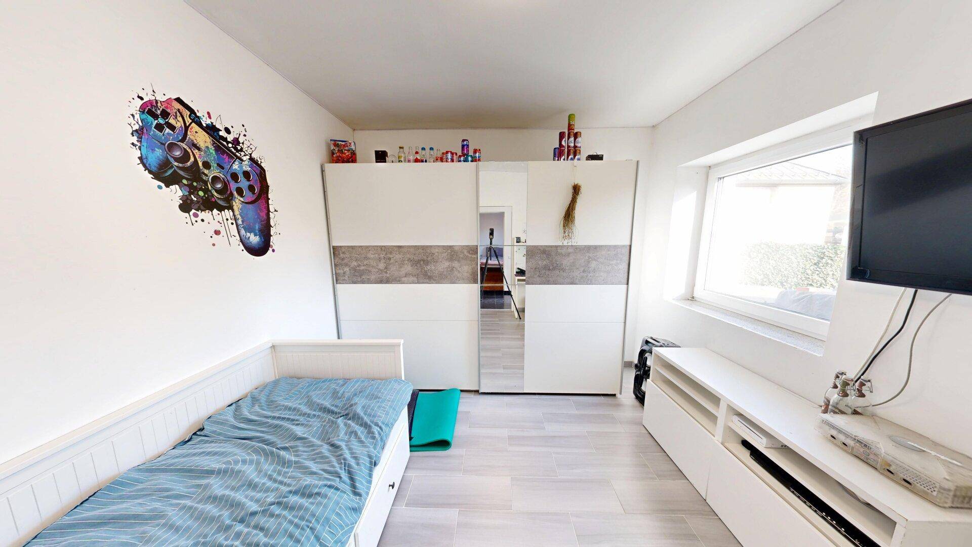 Helles Schlafzimmer mit Einzelbett, großem Kleiderschrank und Fenster für Tageslicht.