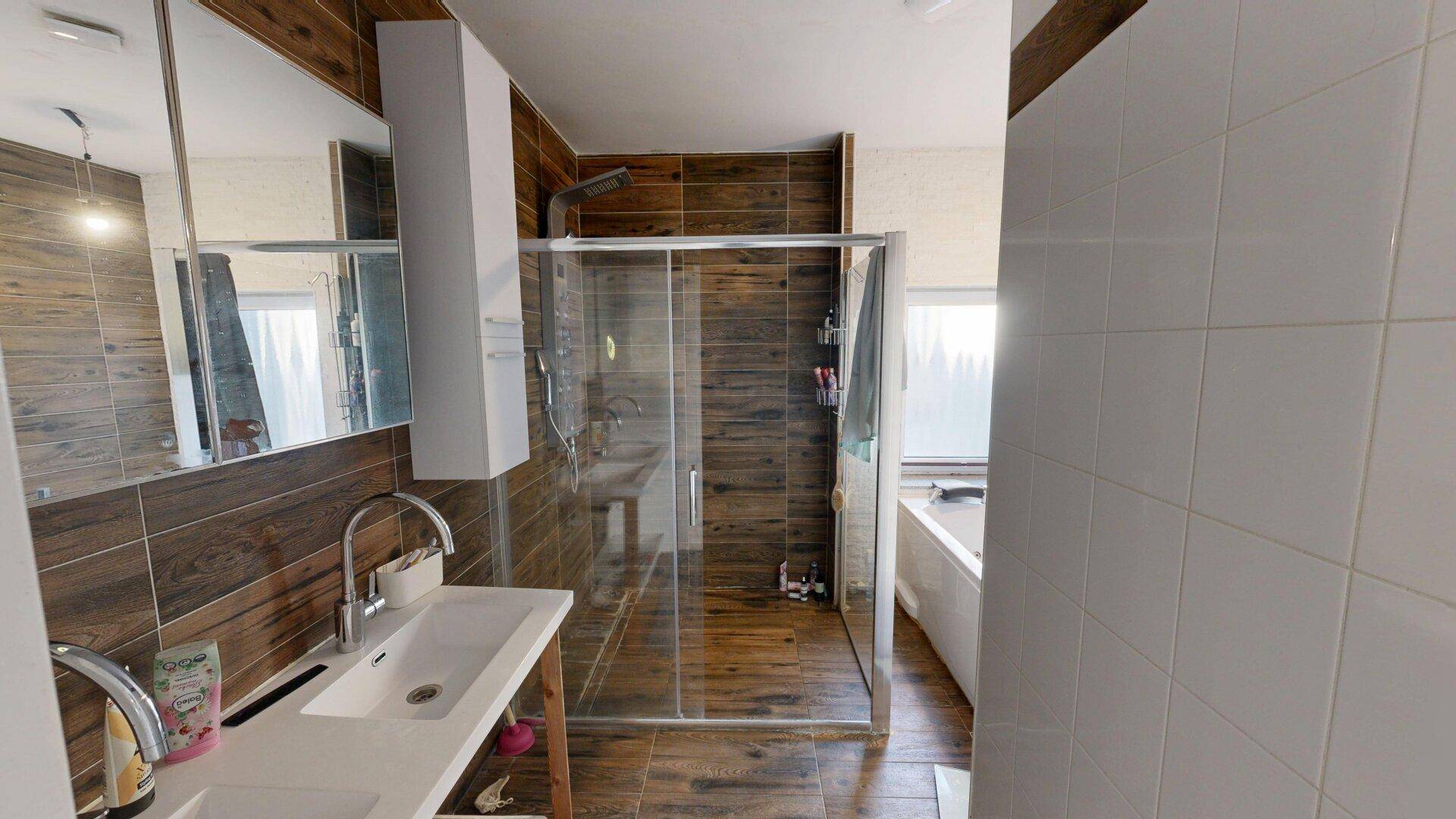 Geräumiges Badezimmer mit Doppelwaschbecken, begehbarer Dusche und Badewanne im Hintergrund.