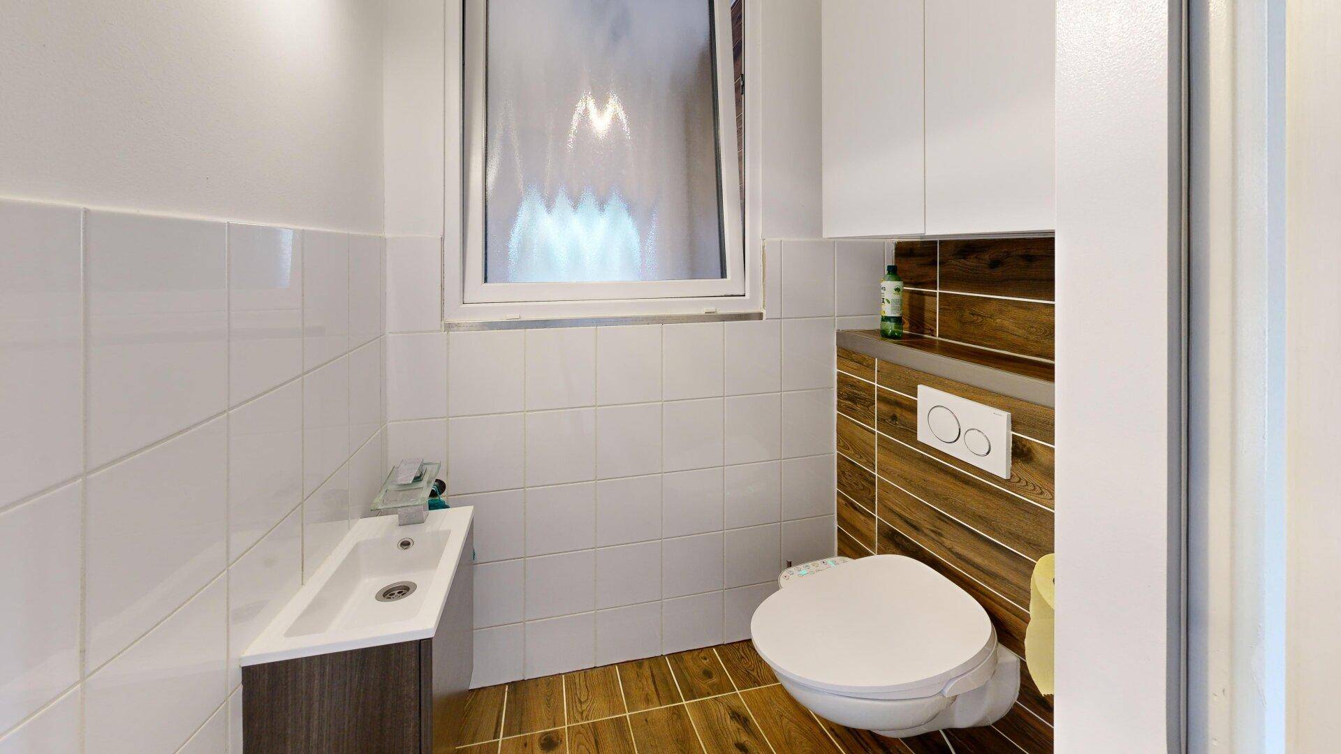 Modernes Gäste-WC mit wandhängendem WC, kleinem Waschbecken und Fenster für Belüftung.