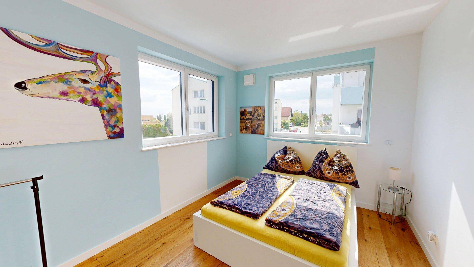 Farbiges Schlafzimmer mit Holzboden, großem Fenster und Blick ins Grüne.