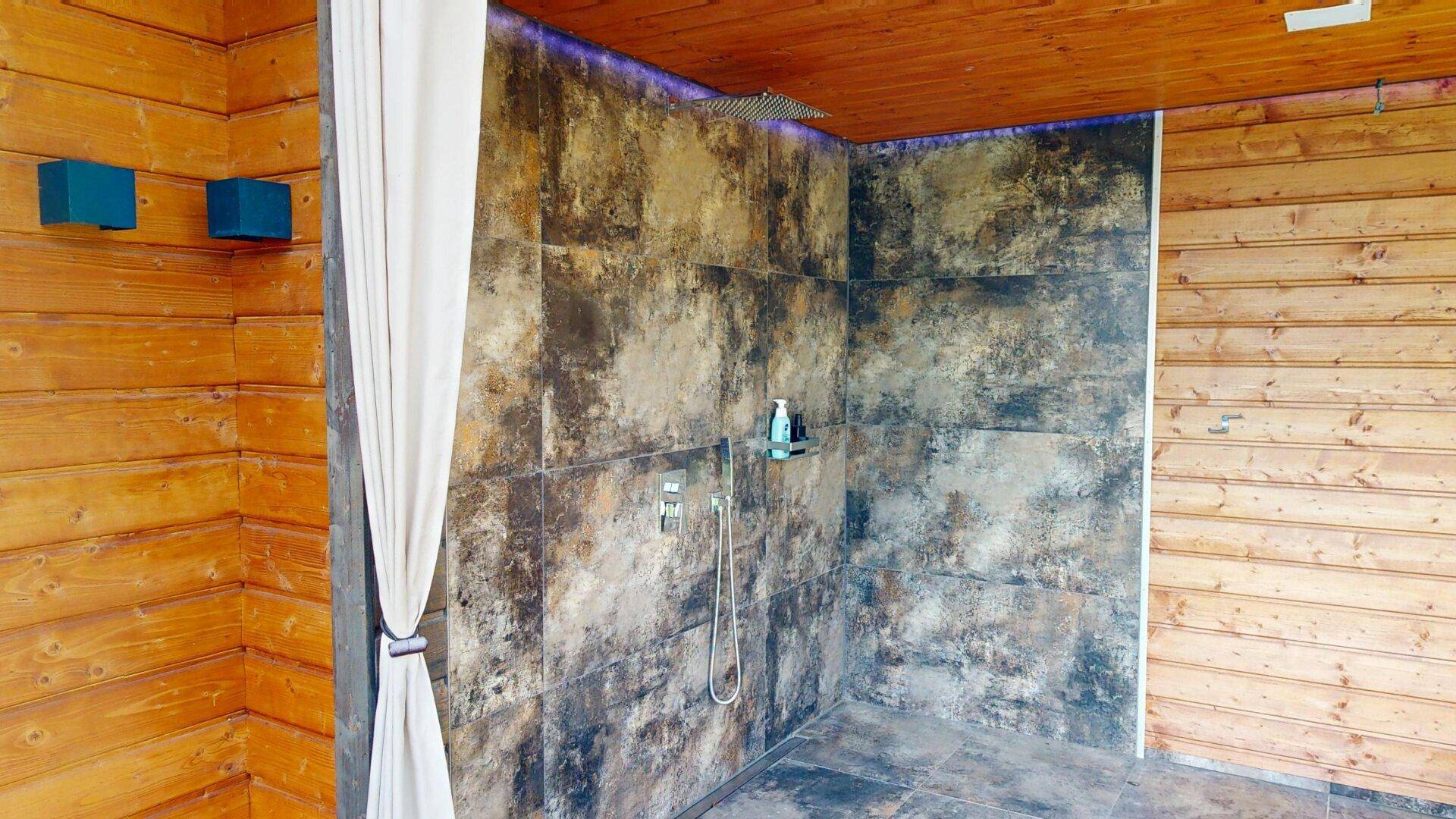 Exklusive Außendusche mit rustikalen Fliesen und Holzverkleidung im Wellnessbereich.
