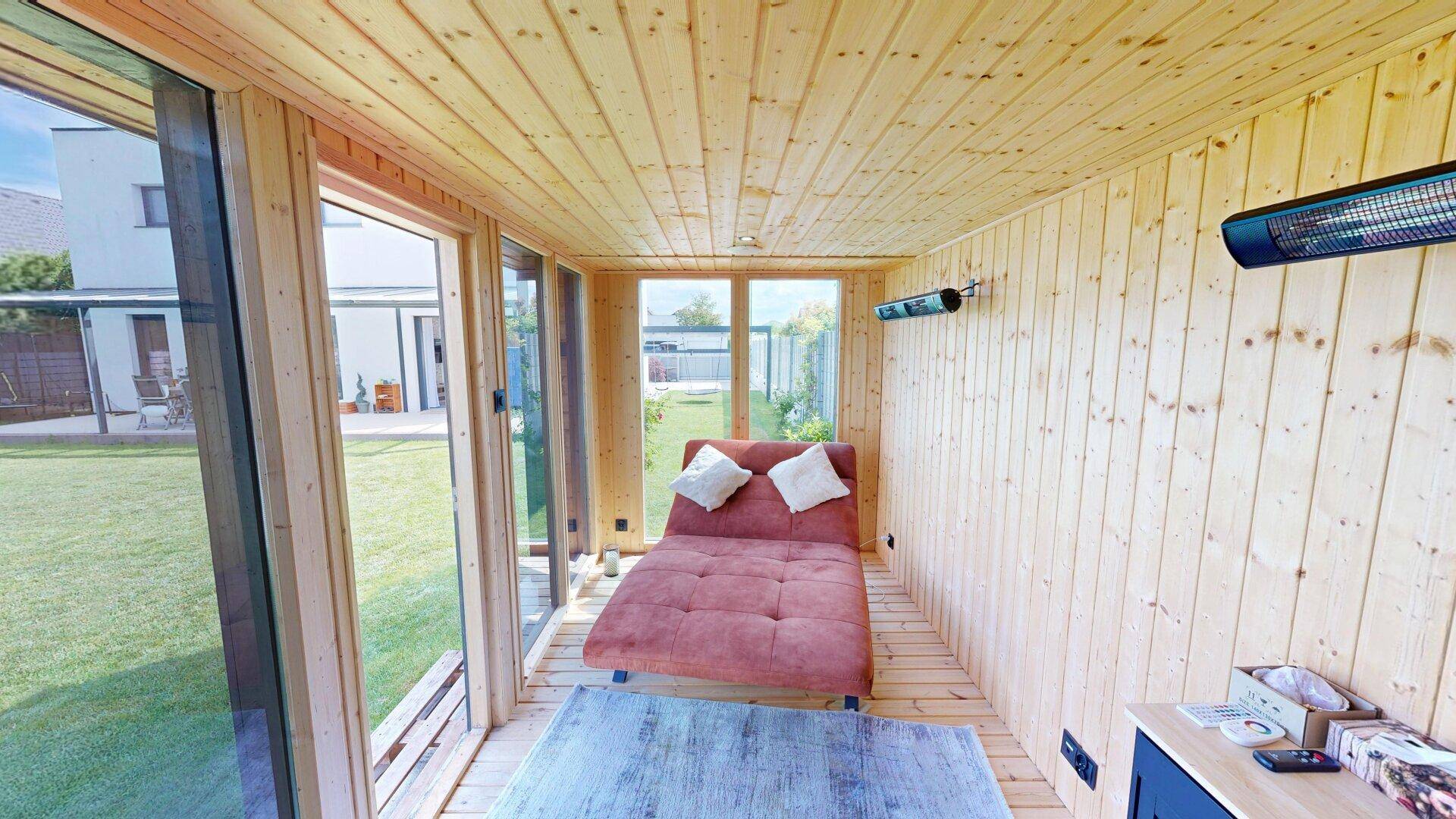 Gemütlicher Ruheraum mit Holzverkleidung, Liege und großen Fenstern zum Garten.