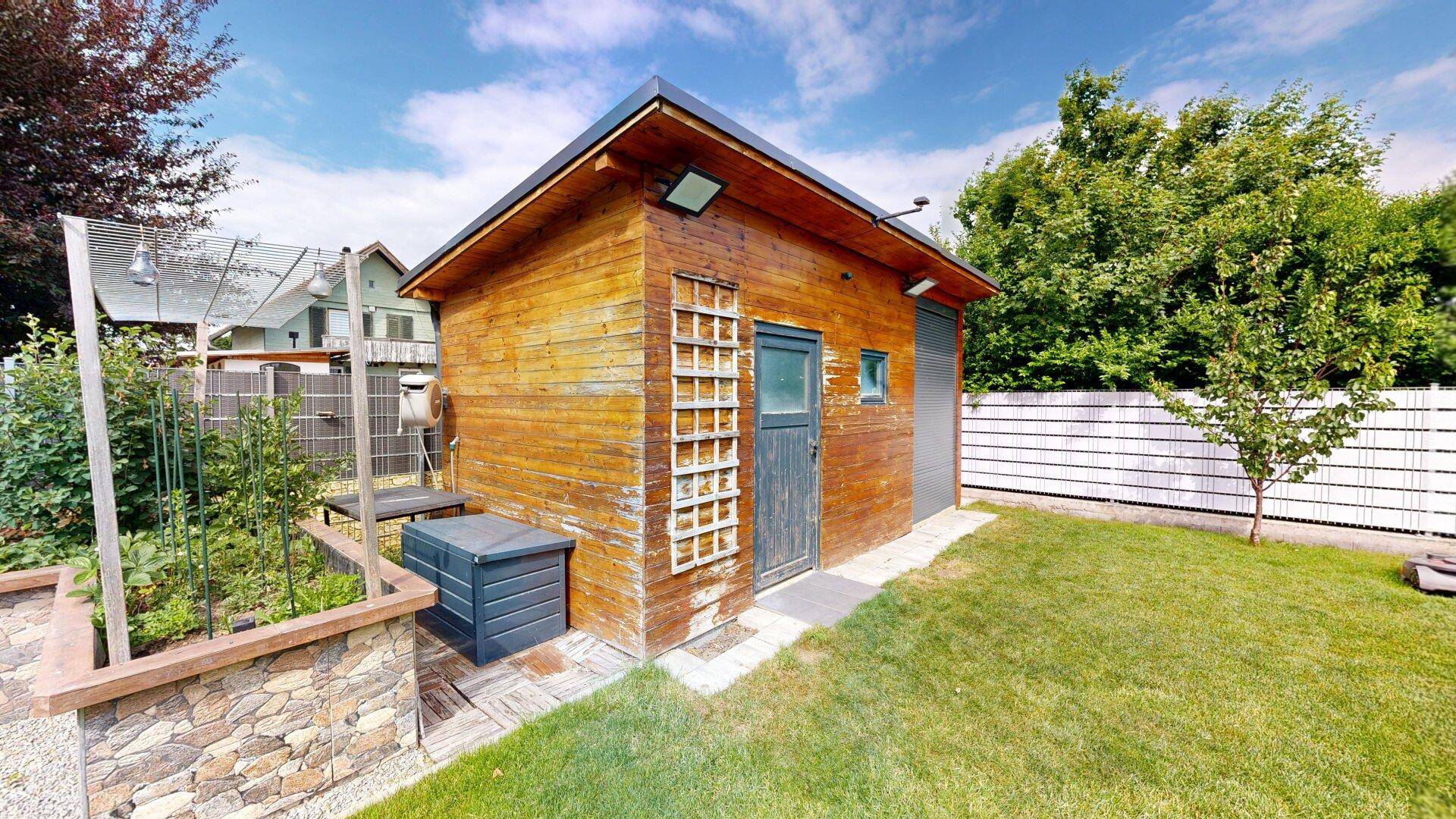 Rustikales Gartenhaus aus Holz mit kleiner Tür und angrenzendem Hochbeet.