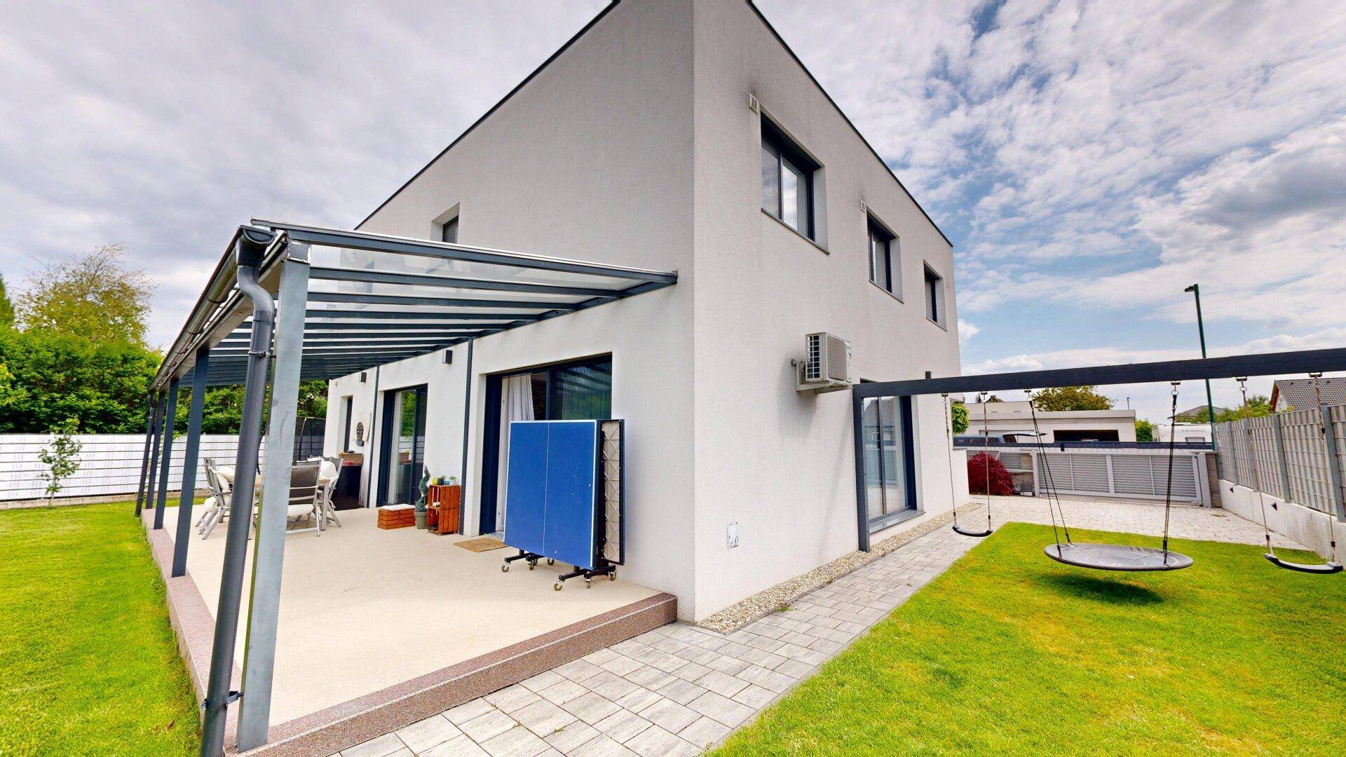 Modernes Haus mit überdachter Terrasse, Schaukel und großem Gartenbereich.