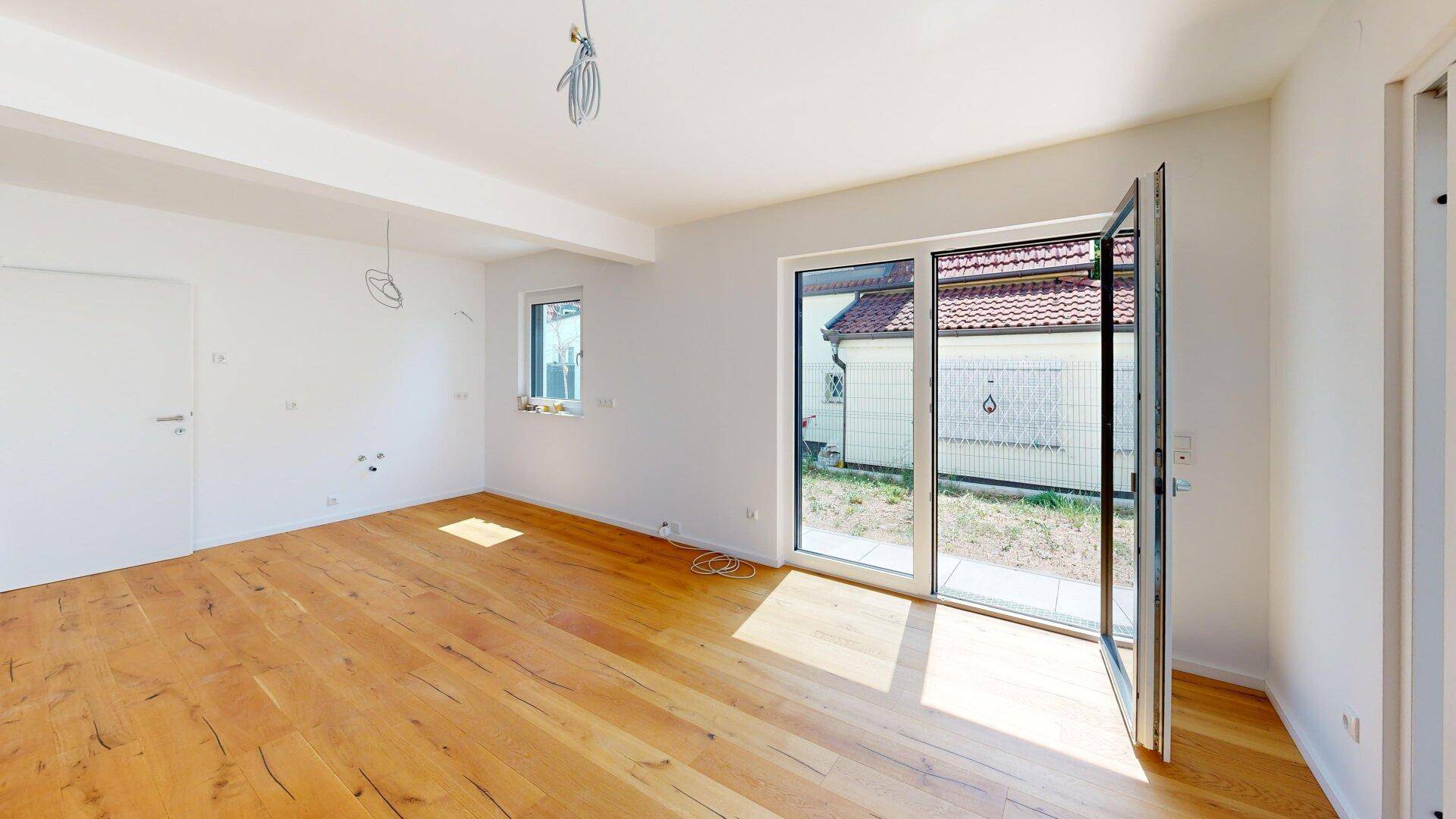 Geräumiges, helles Zimmer mit Holzboden und Zugang zu einem Außenbereich.