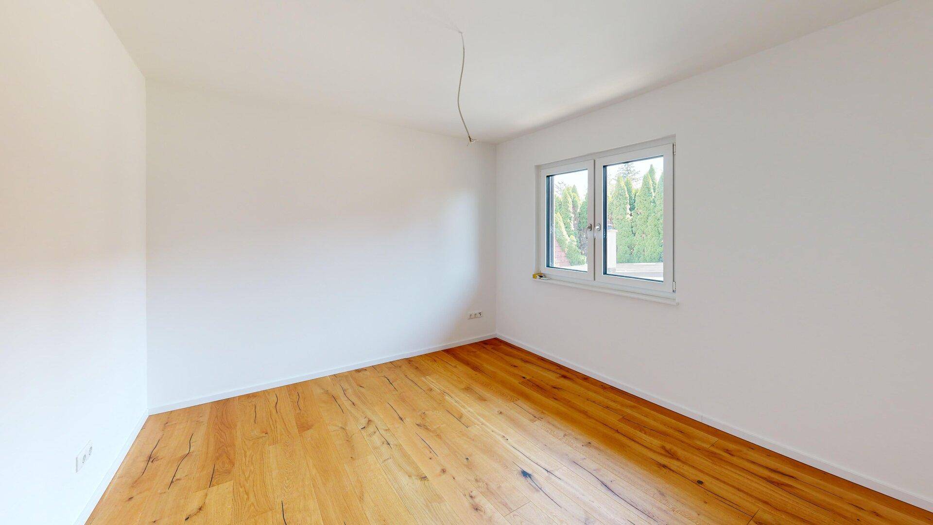 Helles Schlafzimmer mit Holzboden und Blick ins Grüne durch das Fenster.