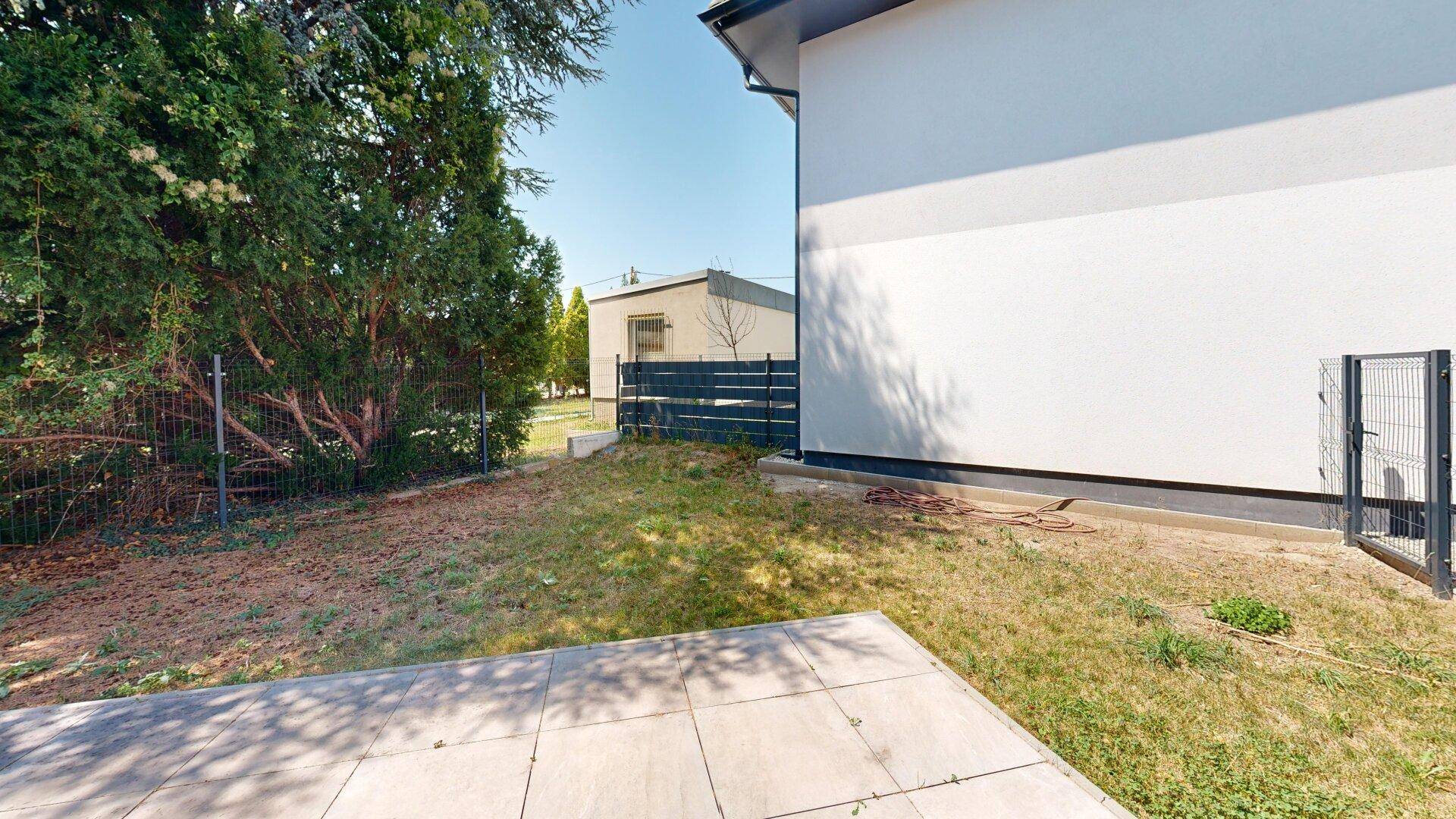 Kleiner Gartenbereich mit Terrasse und Rasenfläche neben dem Neubau.