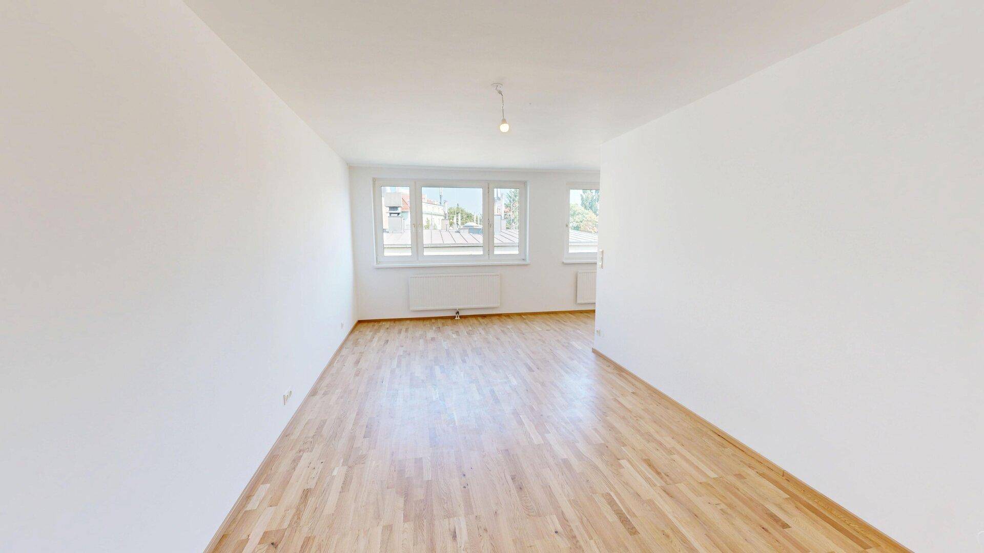 Lichtdurchflutetes Wohnzimmer mit großen Fenstern, Parkettboden und Blick auf die Umgebung.