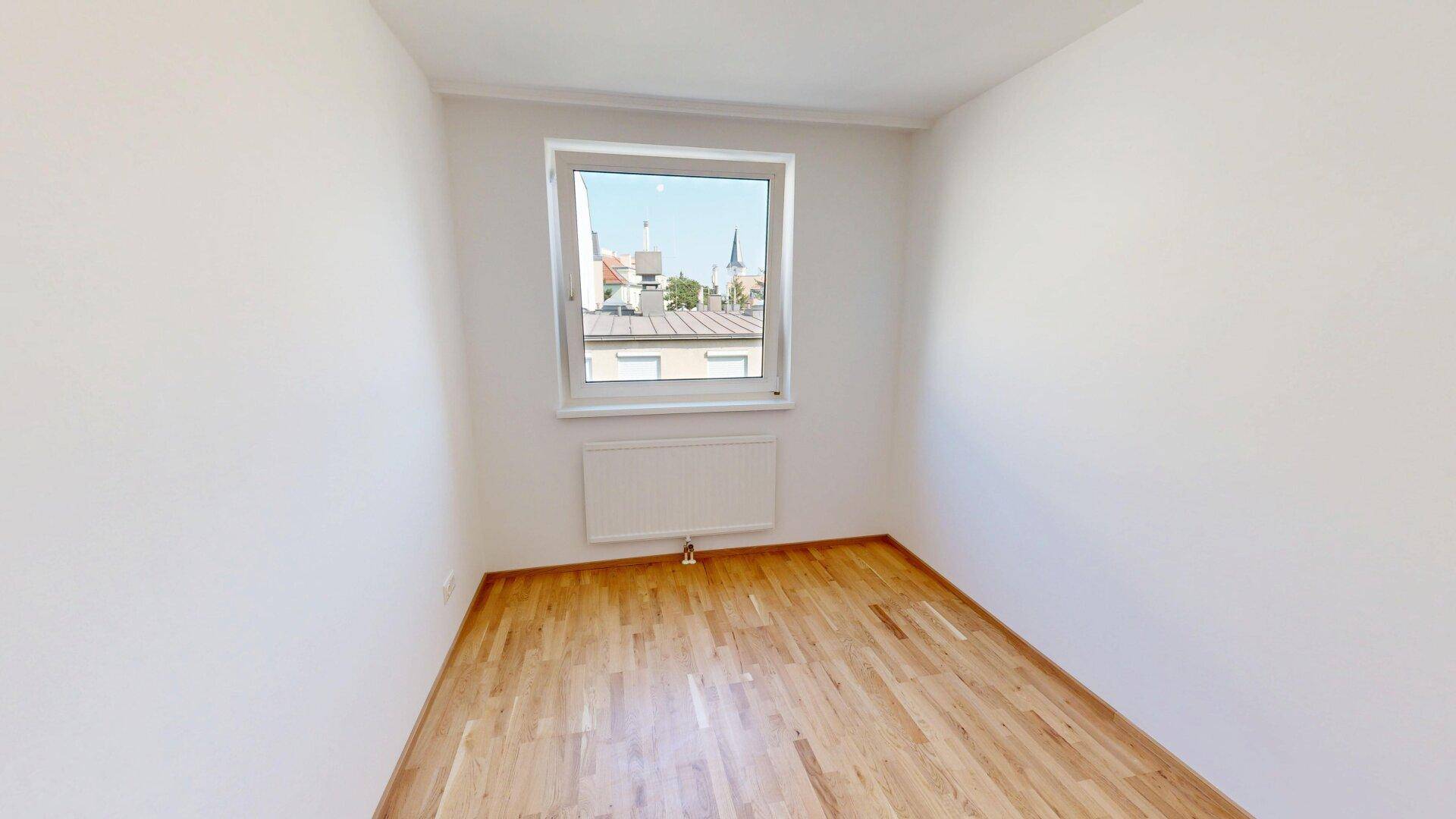 Helles Schlafzimmer mit Parkettboden und einem Fenster, das einen Blick auf die Dächer bietet.