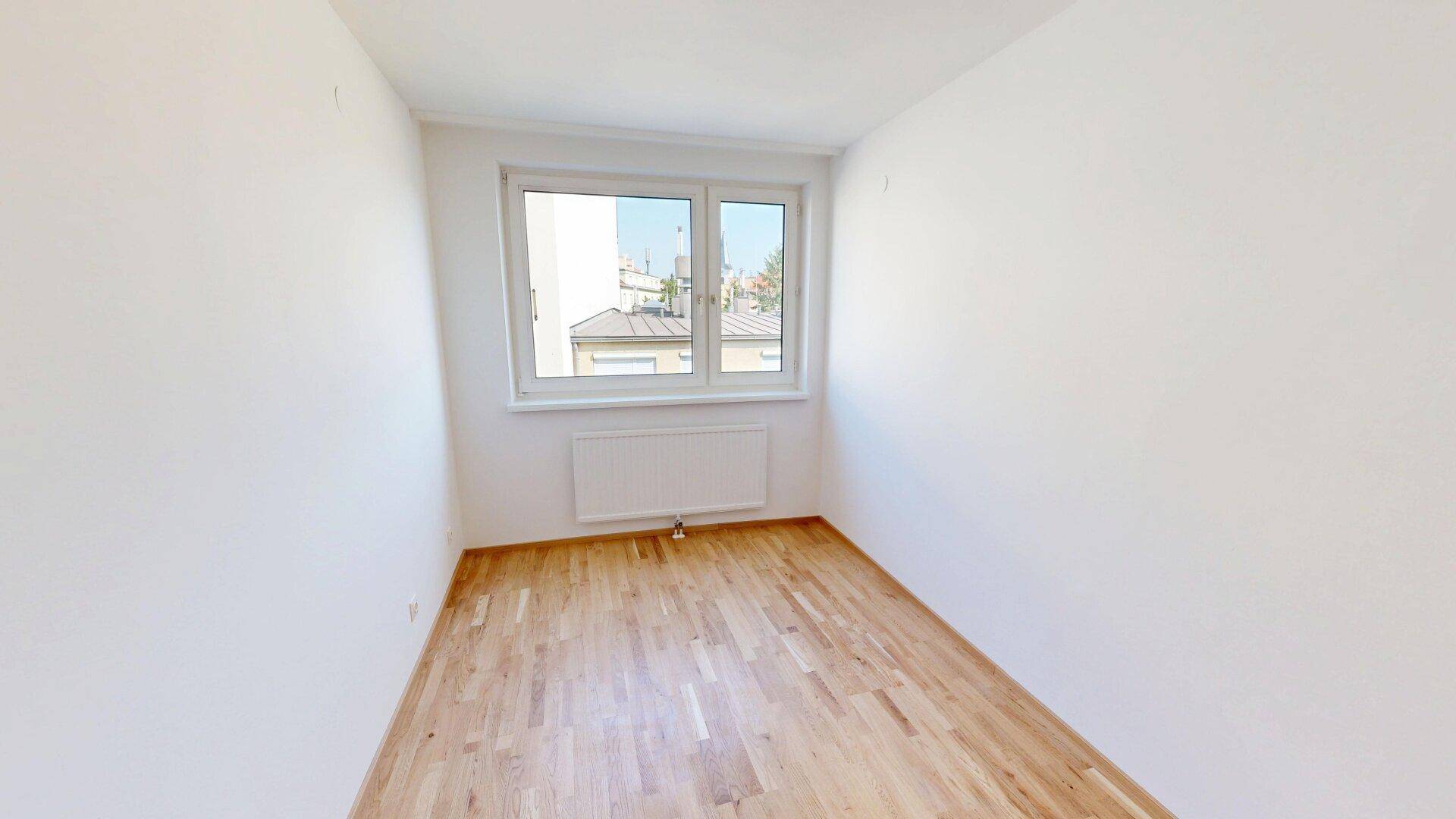 Weiteres helles Schlafzimmer mit Parkettboden und Fenster, das viel Tageslicht hereinlässt.