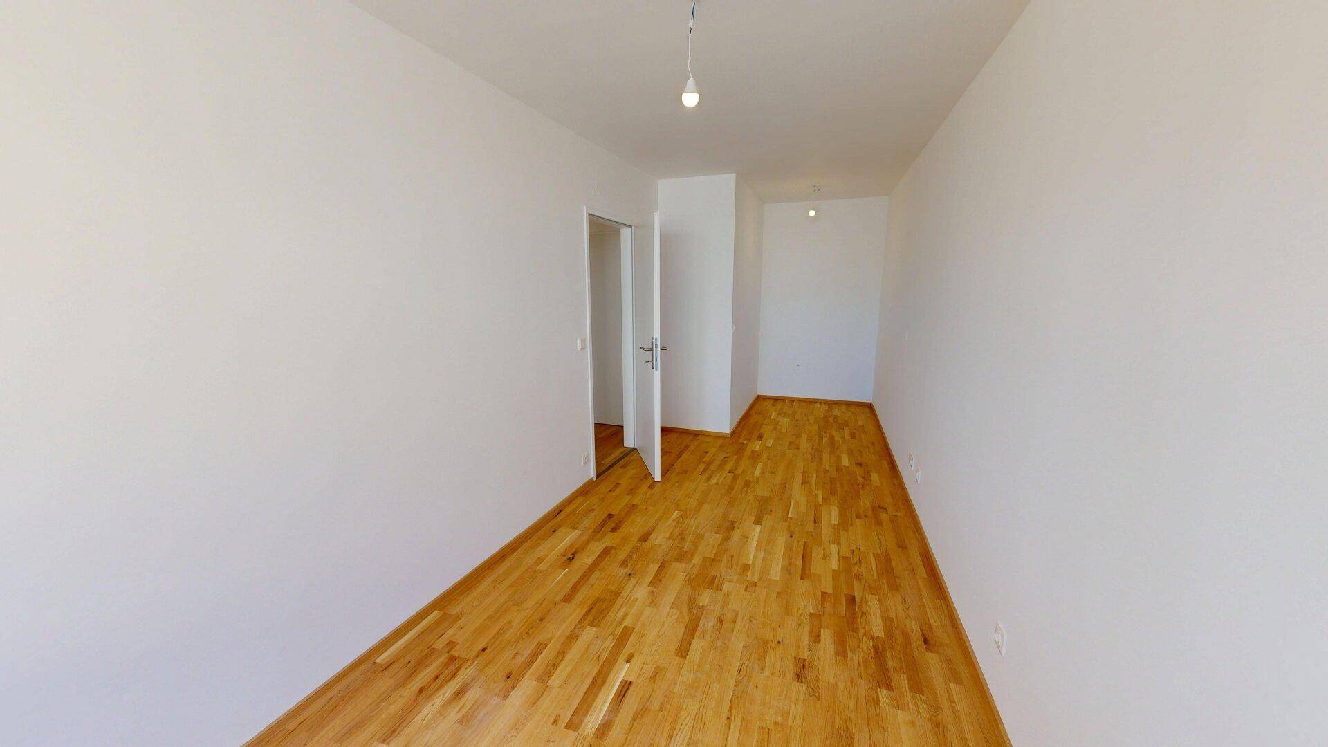 Geräumiges, leeres Zimmer mit Parkettboden und weißen Wänden, ideal für Wohn- oder Essbereich.