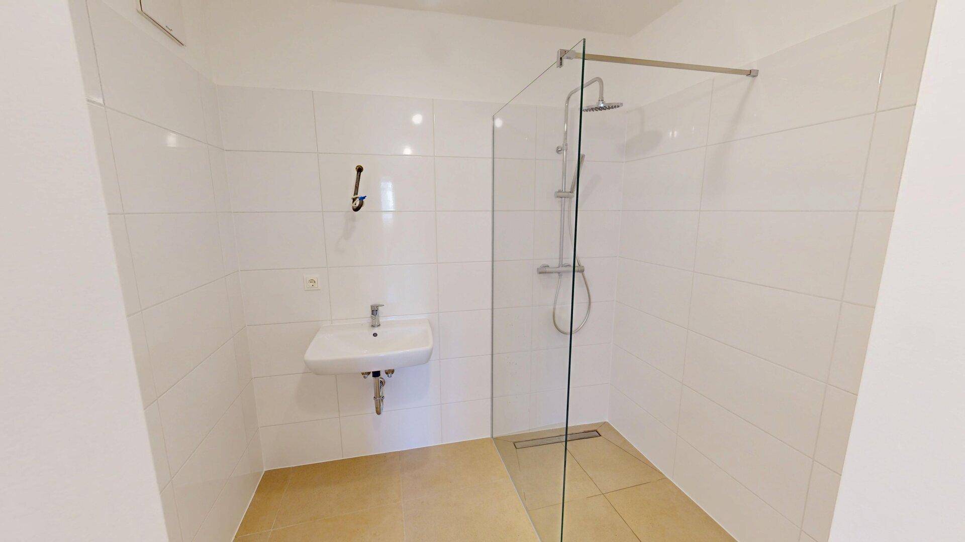 Modernes Badezimmer mit ebenerdiger Dusche, weiß gefliesten Wänden und einem Waschbecken.