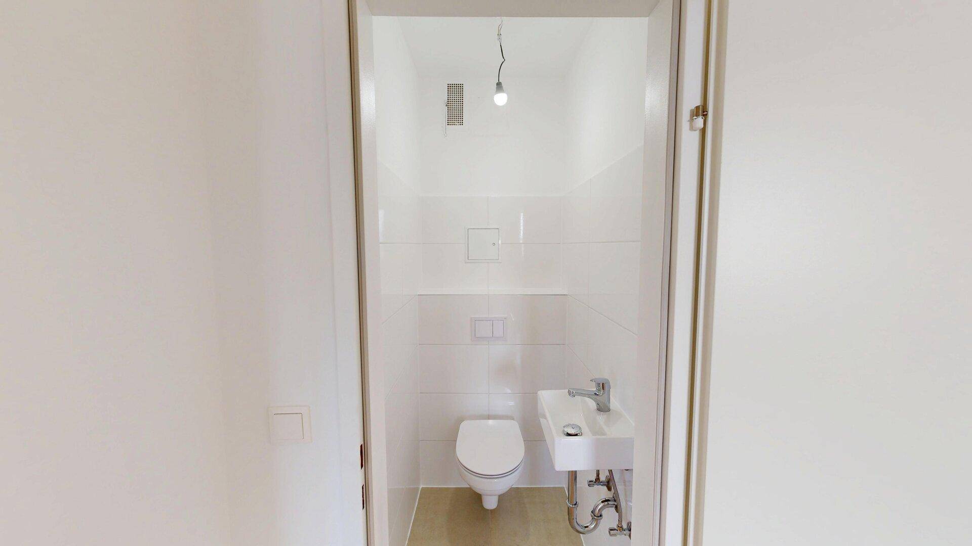 Separates Gäste-WC mit wandhängender Toilette, kleinem Waschbecken und weißen Fliesen.