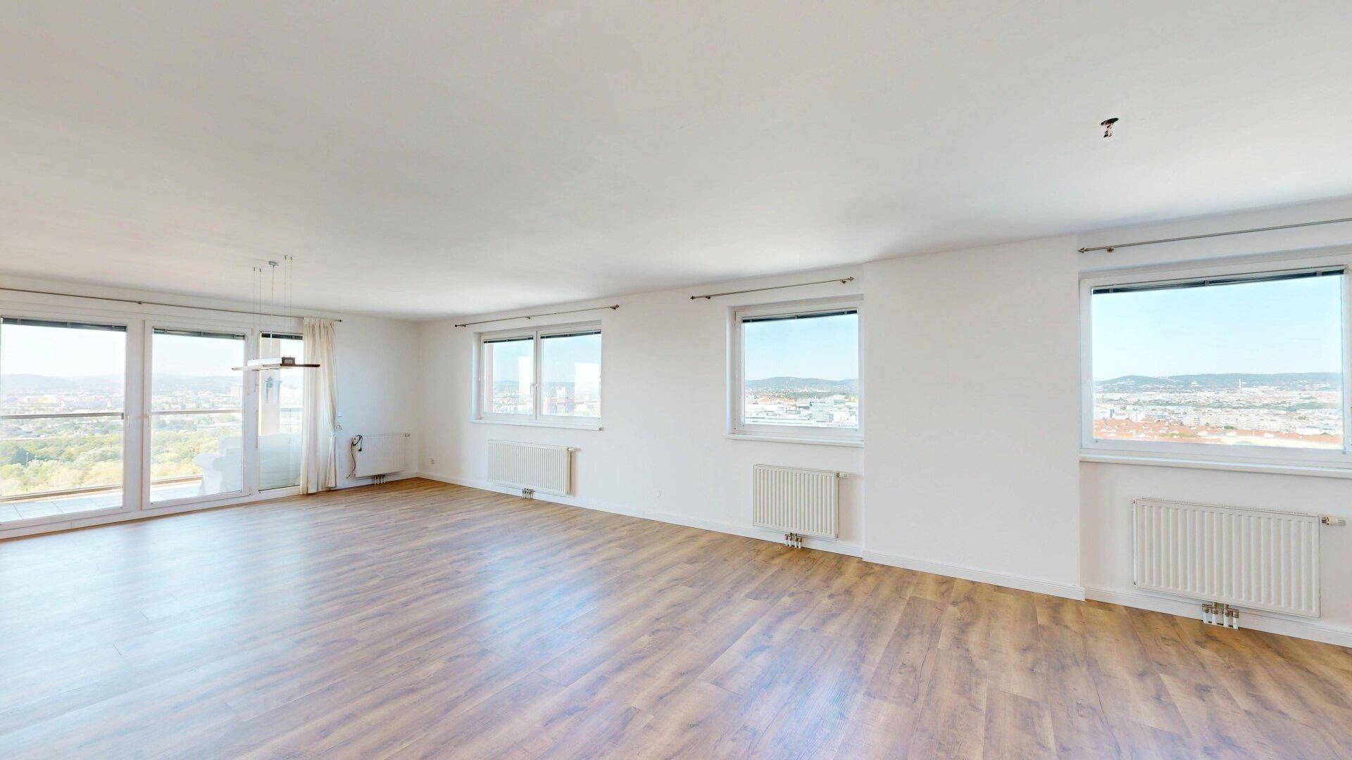 Helles, leeres Wohnzimmer mit Laminatboden, weißen Wänden und weitem Stadtblick.