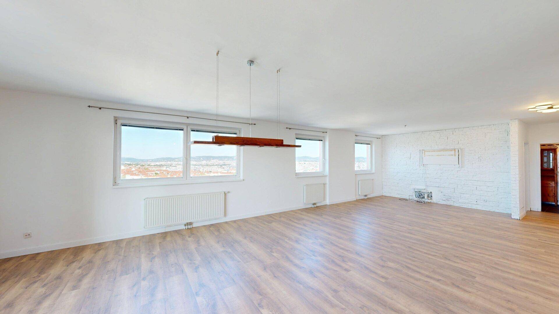 Großes, helles Wohnzimmer mit Laminatboden, einer strukturierten Wand und weitem Ausblick.