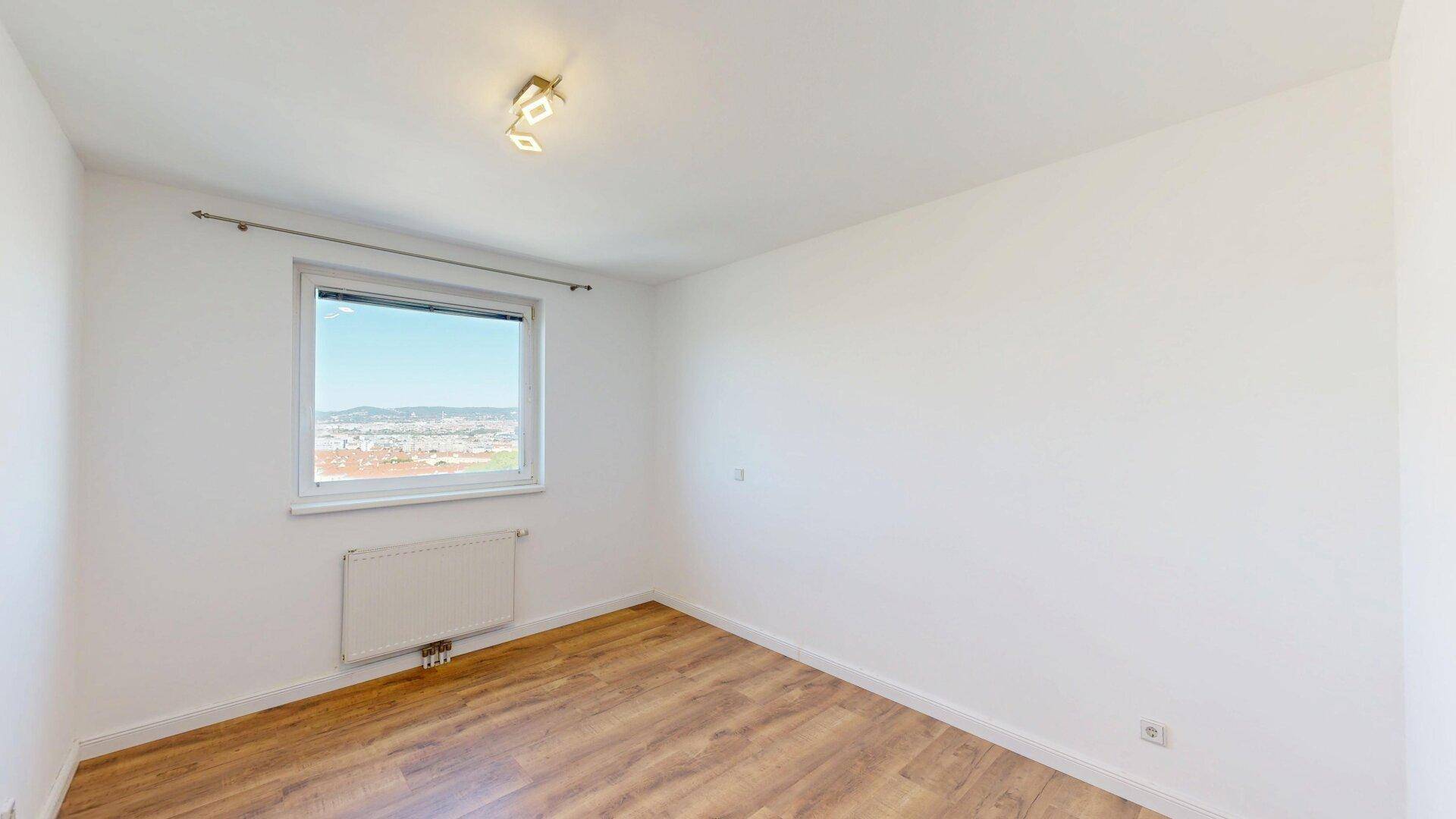 Helles Schlafzimmer mit Laminatboden, weißen Wänden und einem Fenster mit Stadtblick.