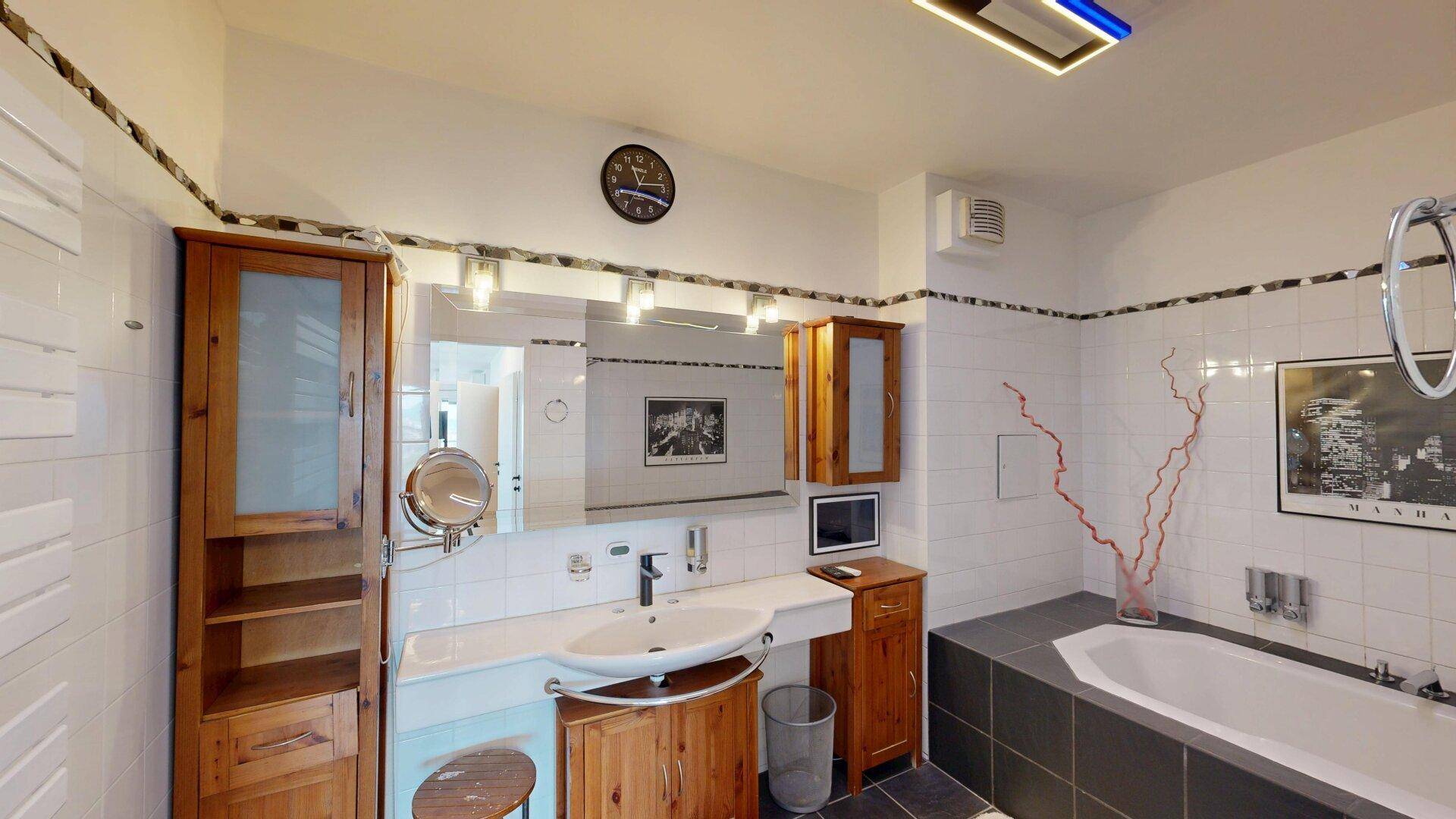 Badezimmer mit eingebauter Badewanne, Holzmöbeln, Einzelwaschbecken und weißen Fliesen.