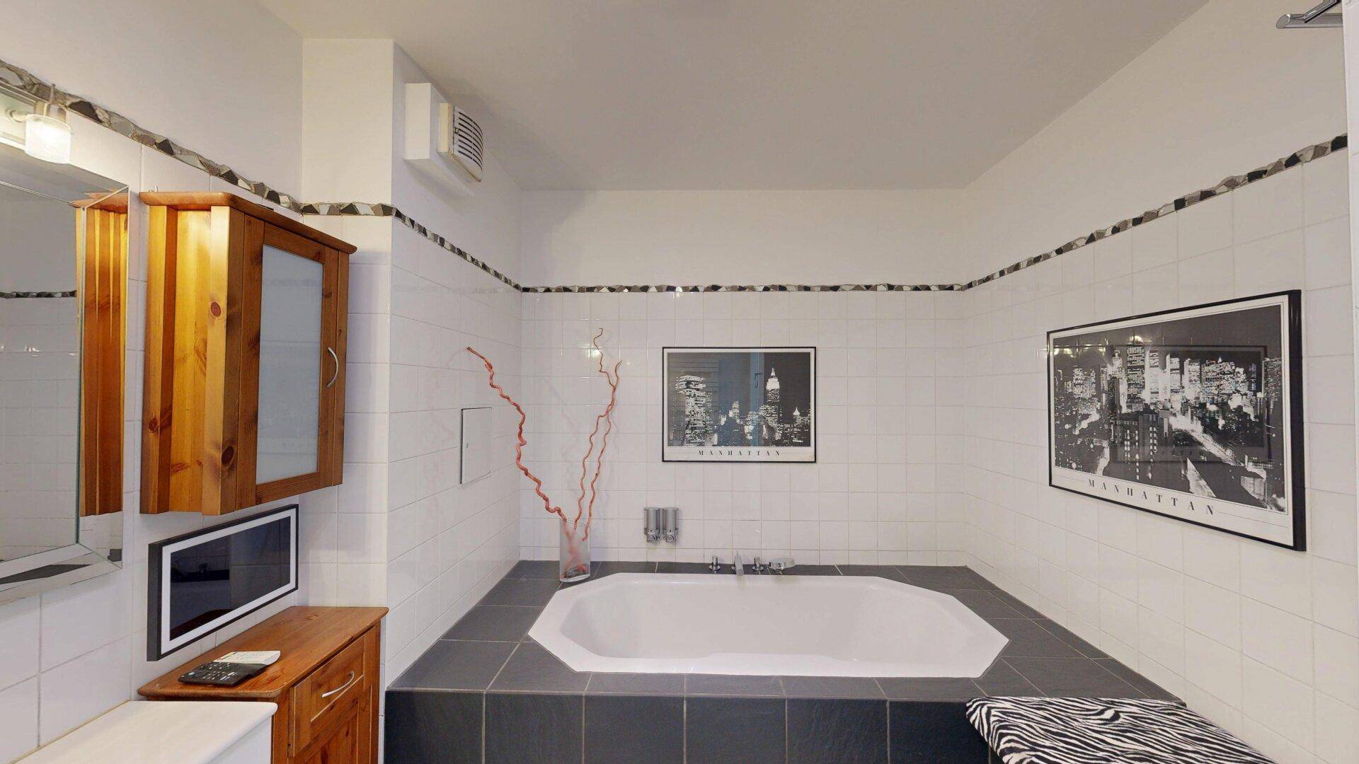 Geräumiges Badezimmer mit großer, eingebauter Badewanne und weiß-schwarzen Fliesen.