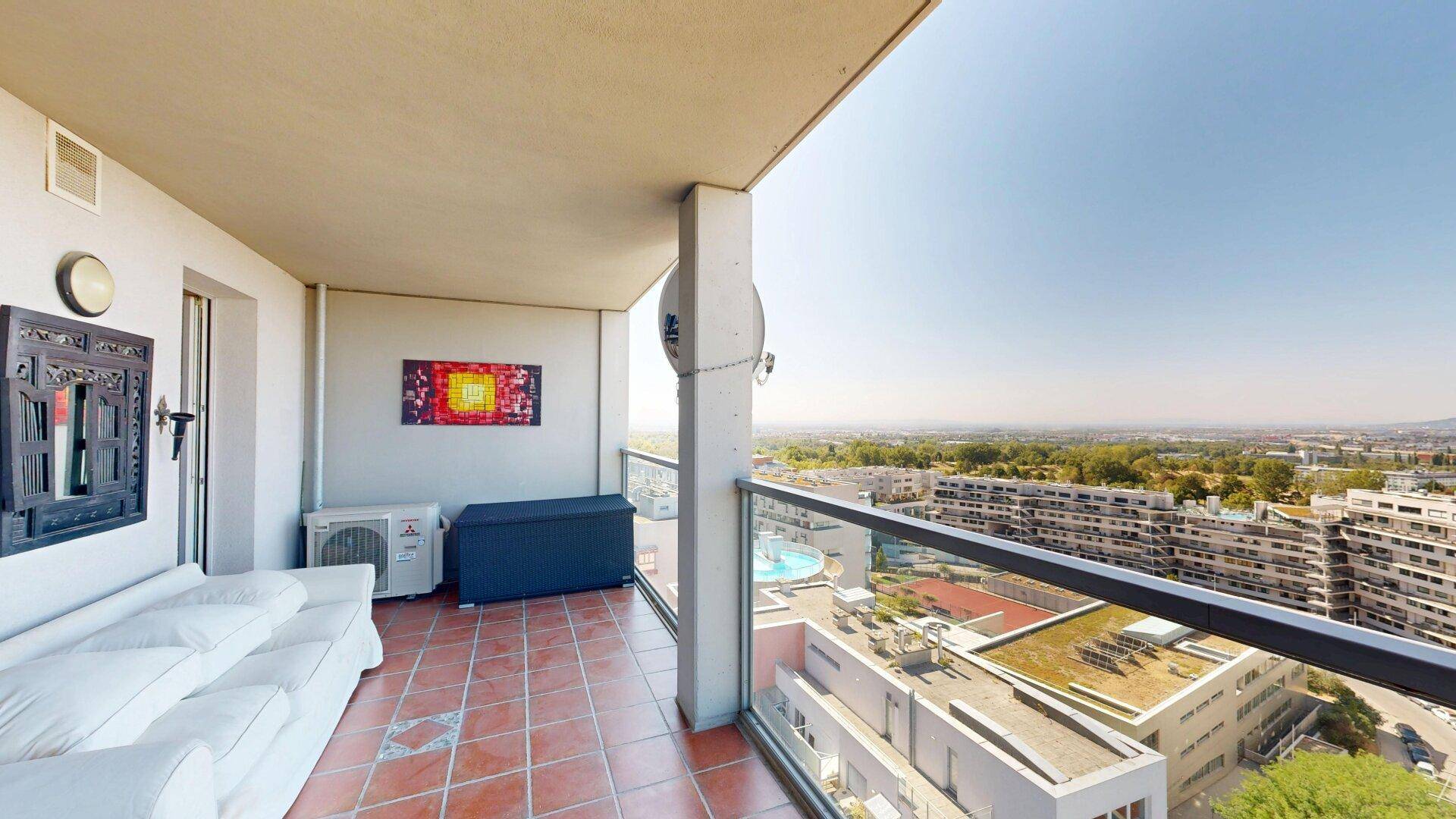 Möblierter Balkon mit Terrakottafliesen, weißem Sofa und Panoramablick über die Stadt.