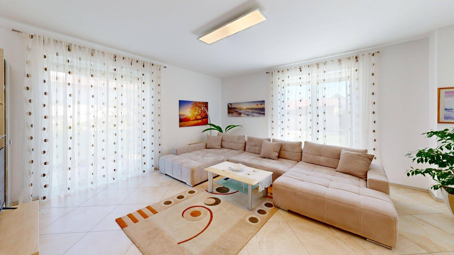 Helles Wohnzimmer mit großem Ecksofa, Fliesenboden und bodentiefen Fenstern für viel Tageslicht.