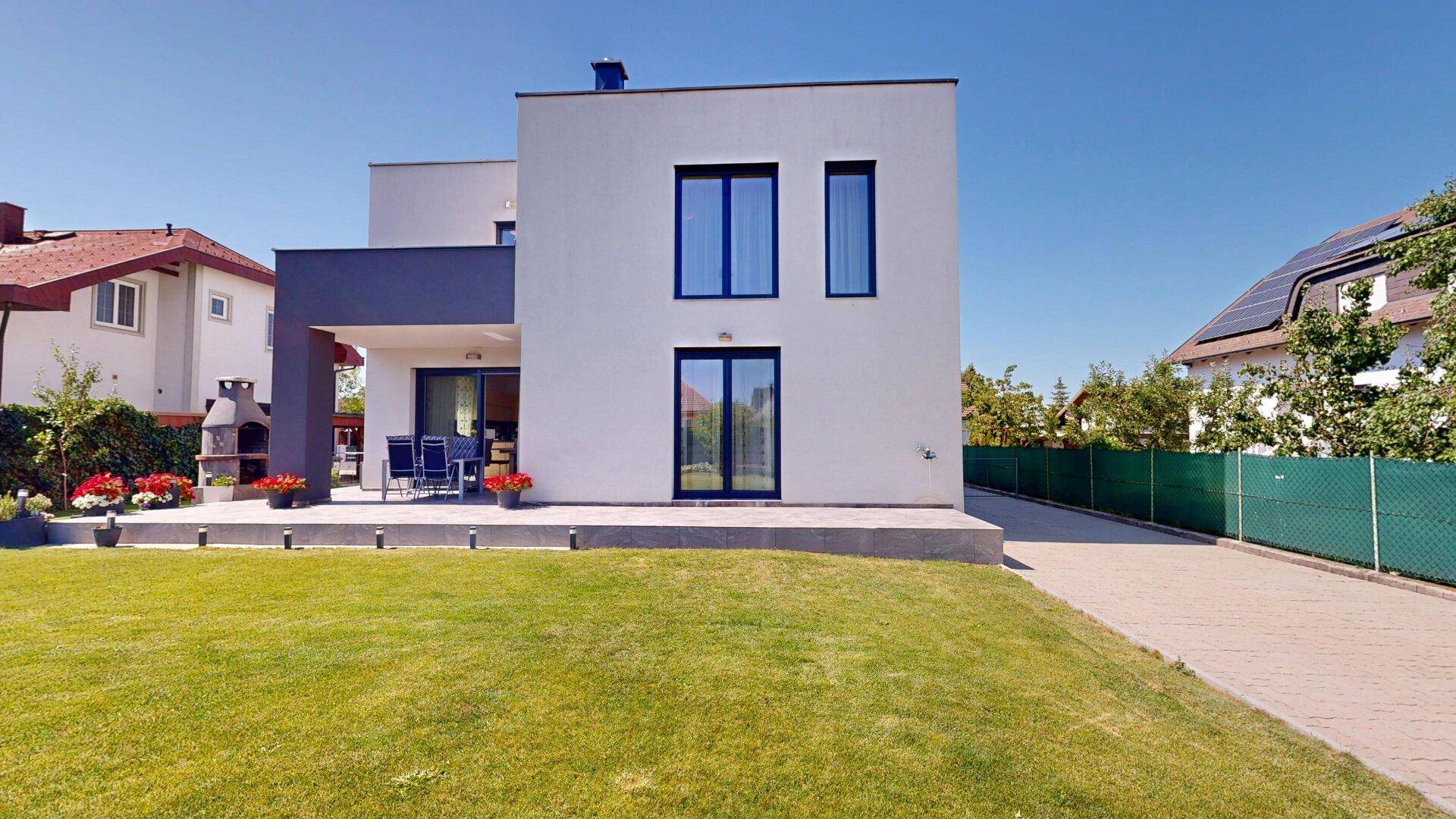 Moderne Hausfassade mit großen Fenstern und Zugang zum Garten, die viel Licht hereinlässt.