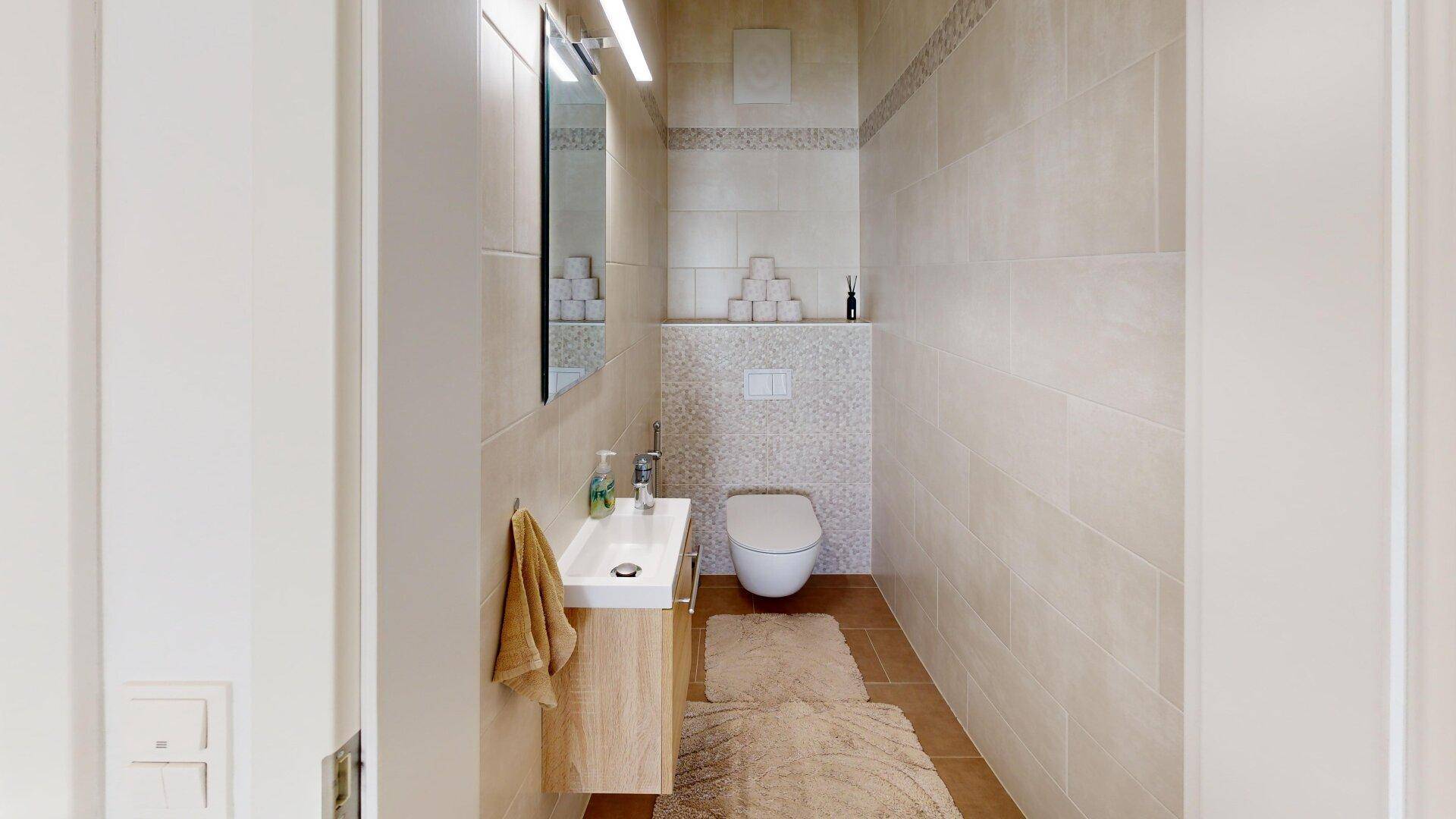 Kleines Gäste-WC mit wandmontierter Toilette und Einzelwaschbecken in neutralen Farbtönen.