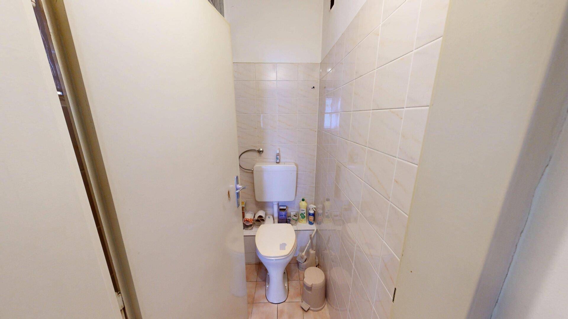 Kleines separates WC mit Toilette und gefliesten Wänden, funktional und einfach gehalten für Gäste.